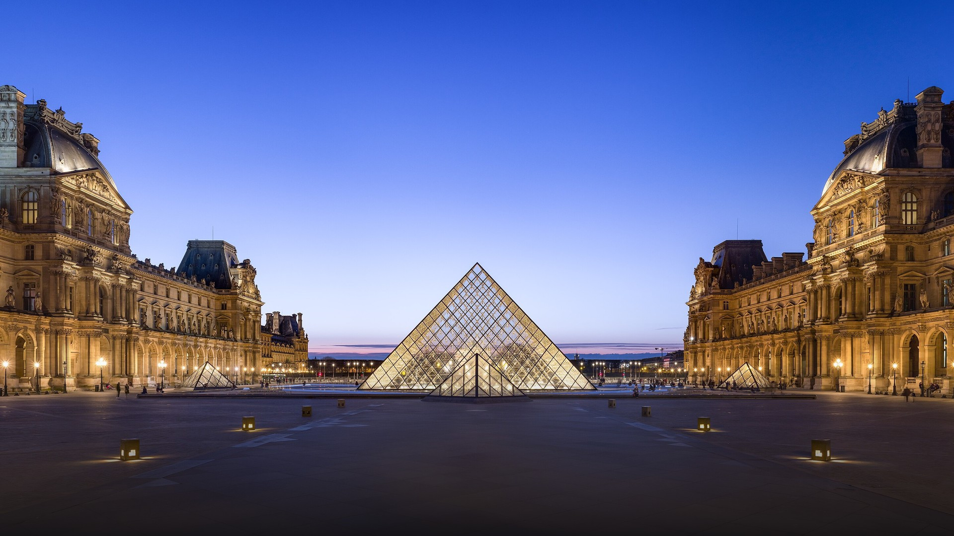 The iconic I.M. Pei glass pyramid and historic palace wings of the Louvre illuminated at dusk.
