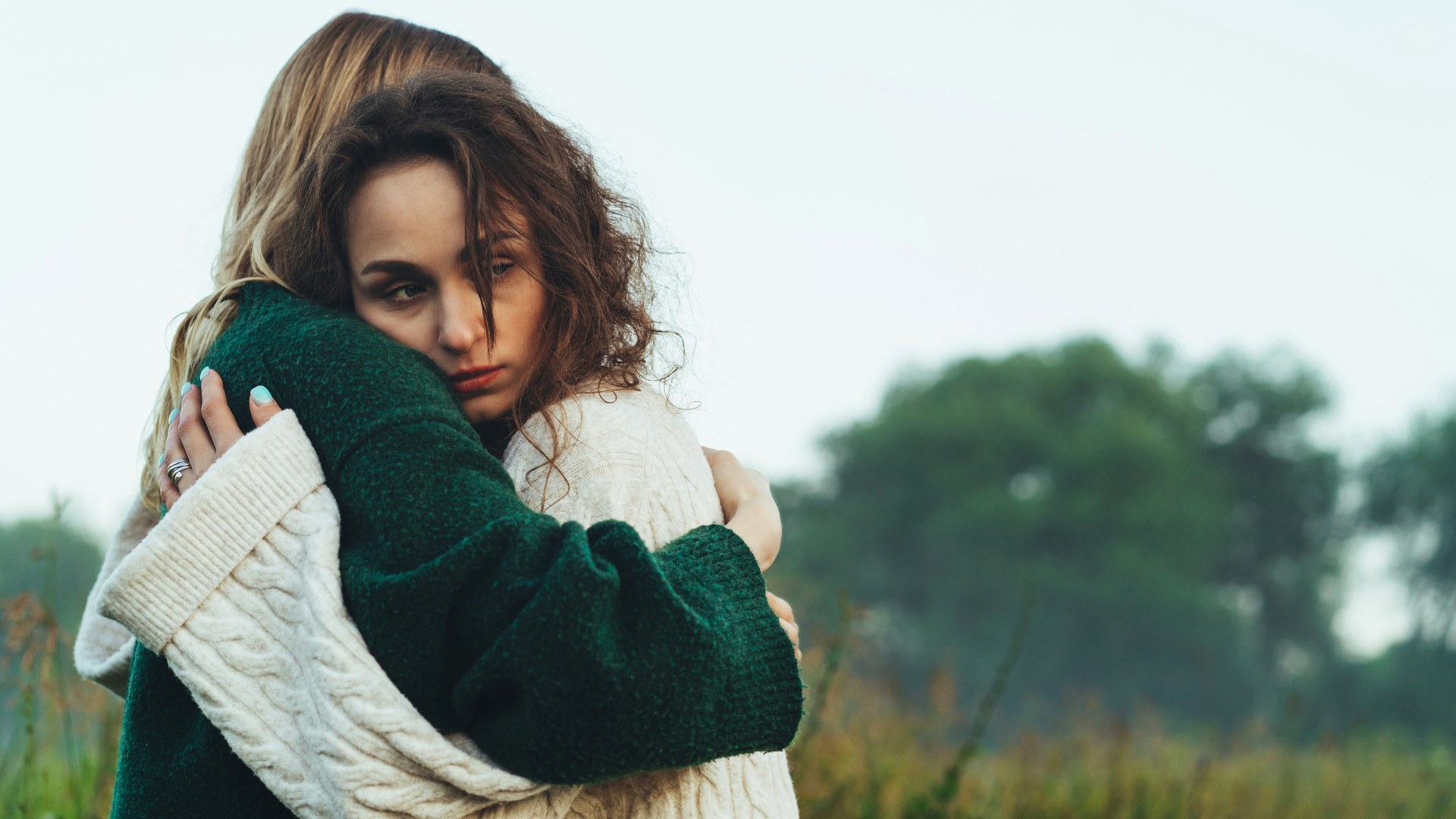 A woman hugging another woman with a detached expression