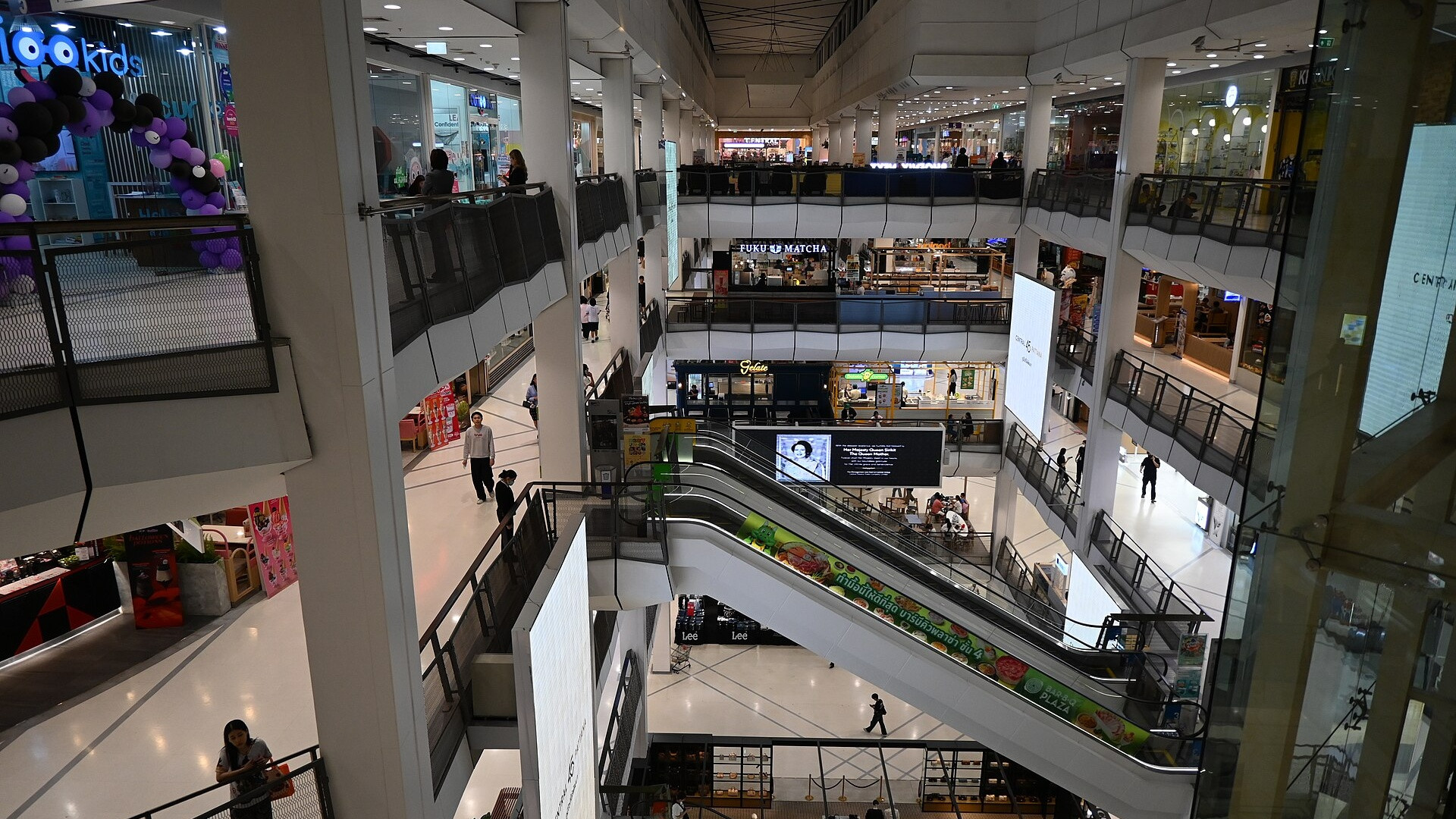 Multi-level shopping mall promenade with shoppers and retail stores.