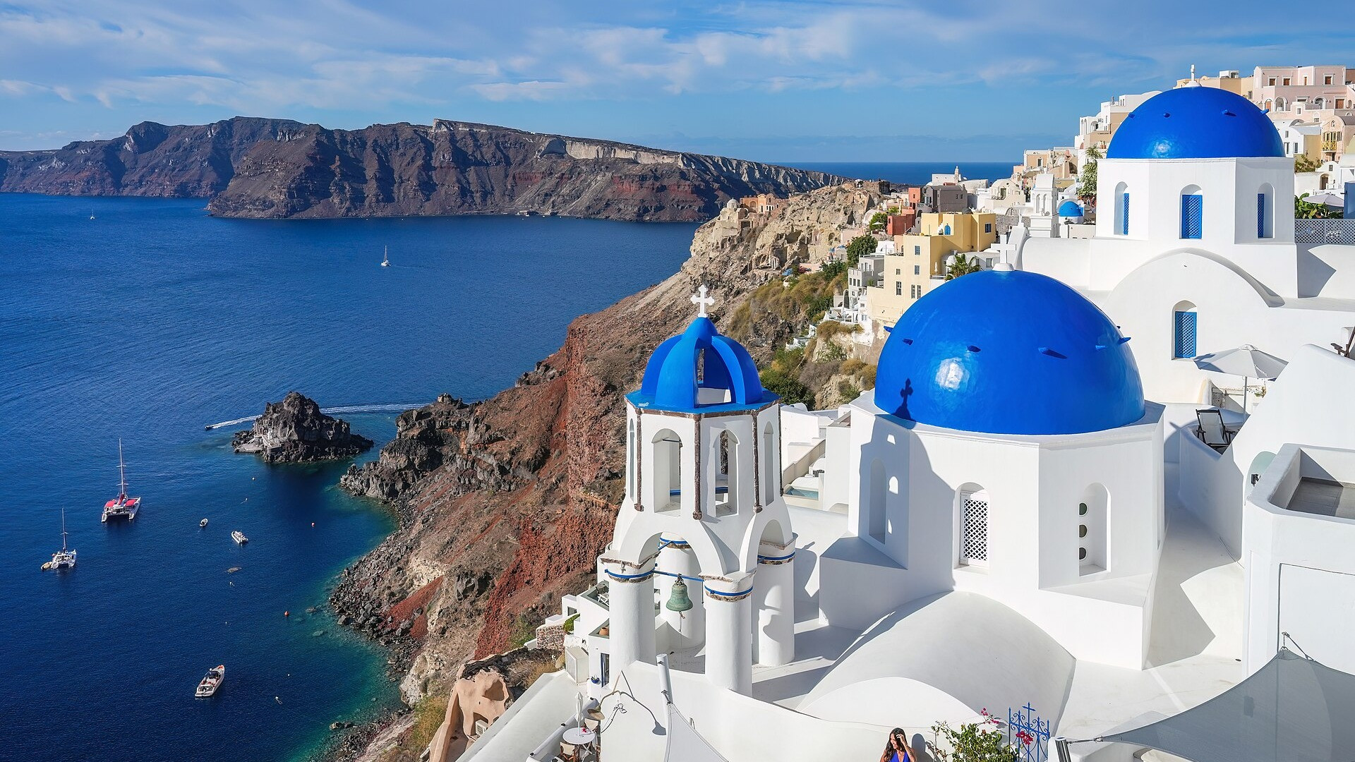 Iconic blue-domed churches and whitewashed bell towers of Oia perched high above the Aegean Sea caldera.