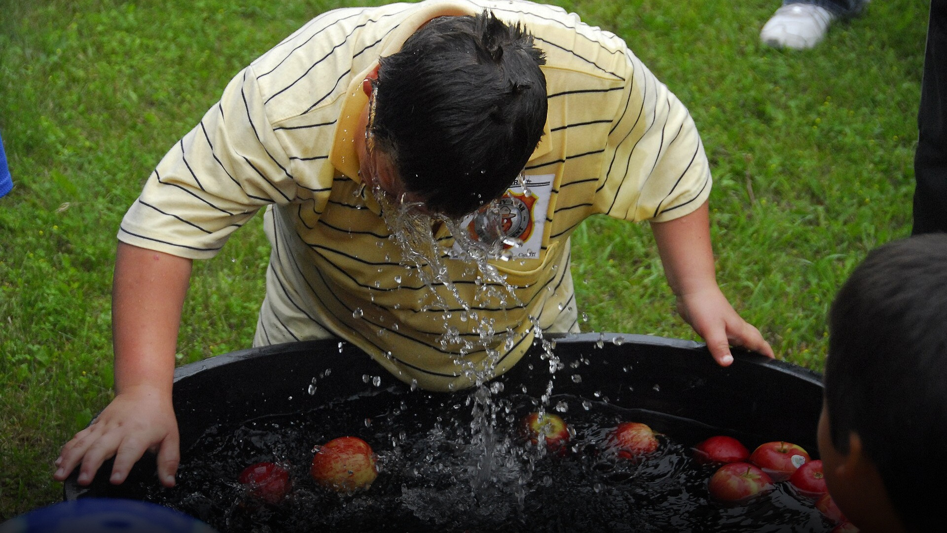 Party attendees gathered around a galvanized water tub bobbing for floating red apples.