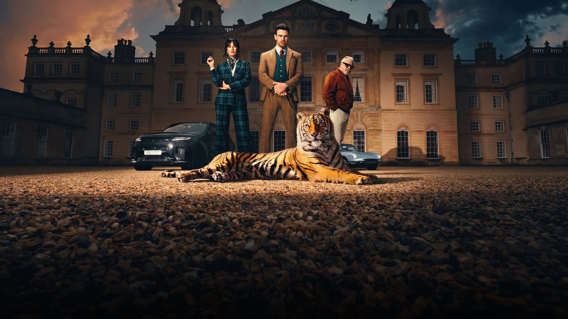 Theo James and Kaya Scodelario standing stylishly before an English country manor with a tiger in foreground.