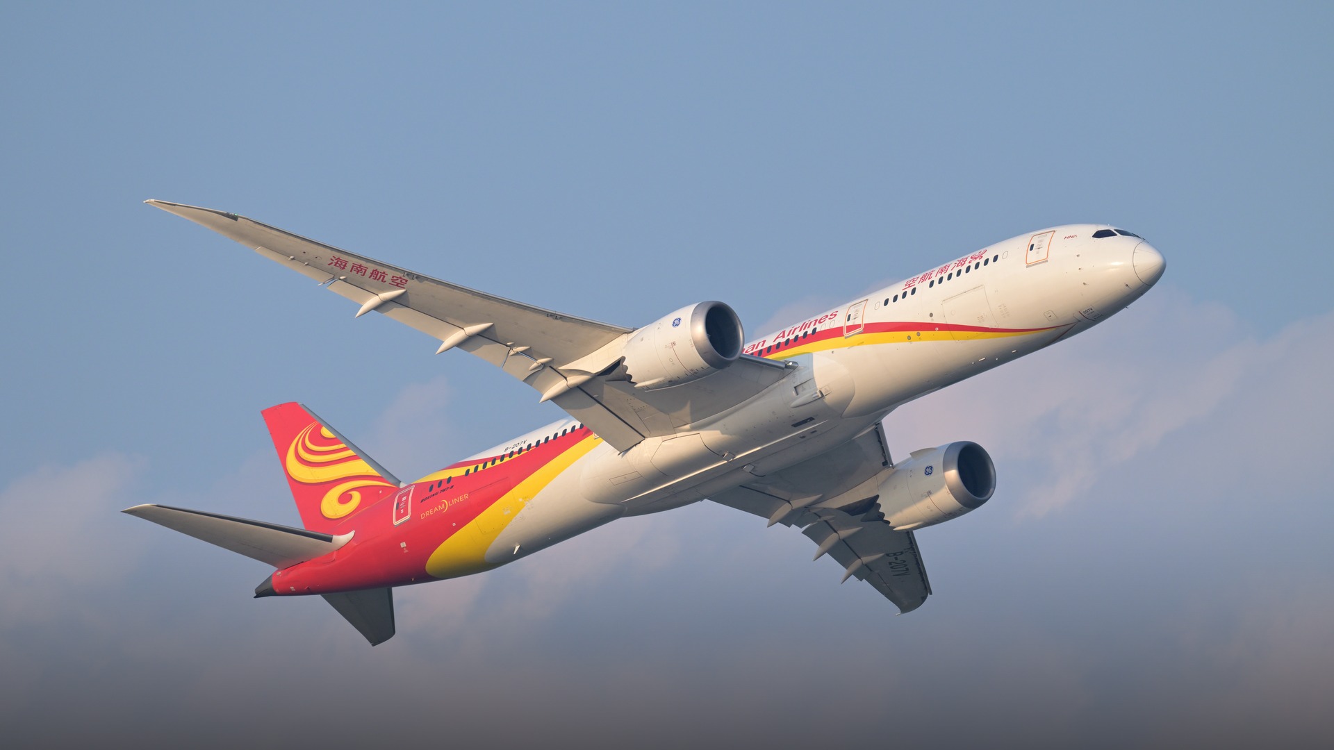 A vibrant red and gold Hainan Airlines Boeing 787-9 Dreamliner climbing smoothly after takeoff.