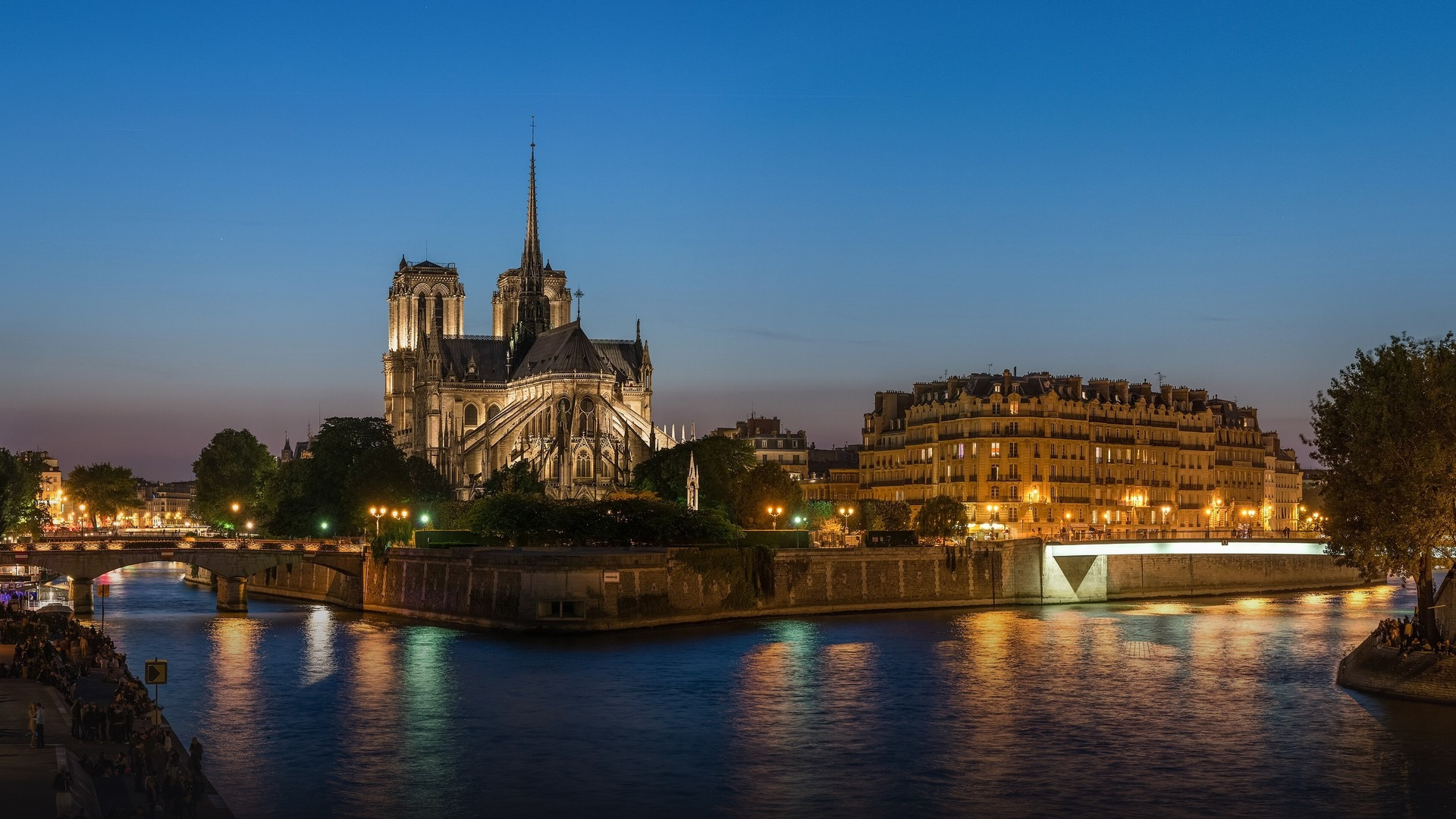 The soaring western facade, twin towers, and central rose window of Notre-Dame de Paris alongside the evening Seine river view.