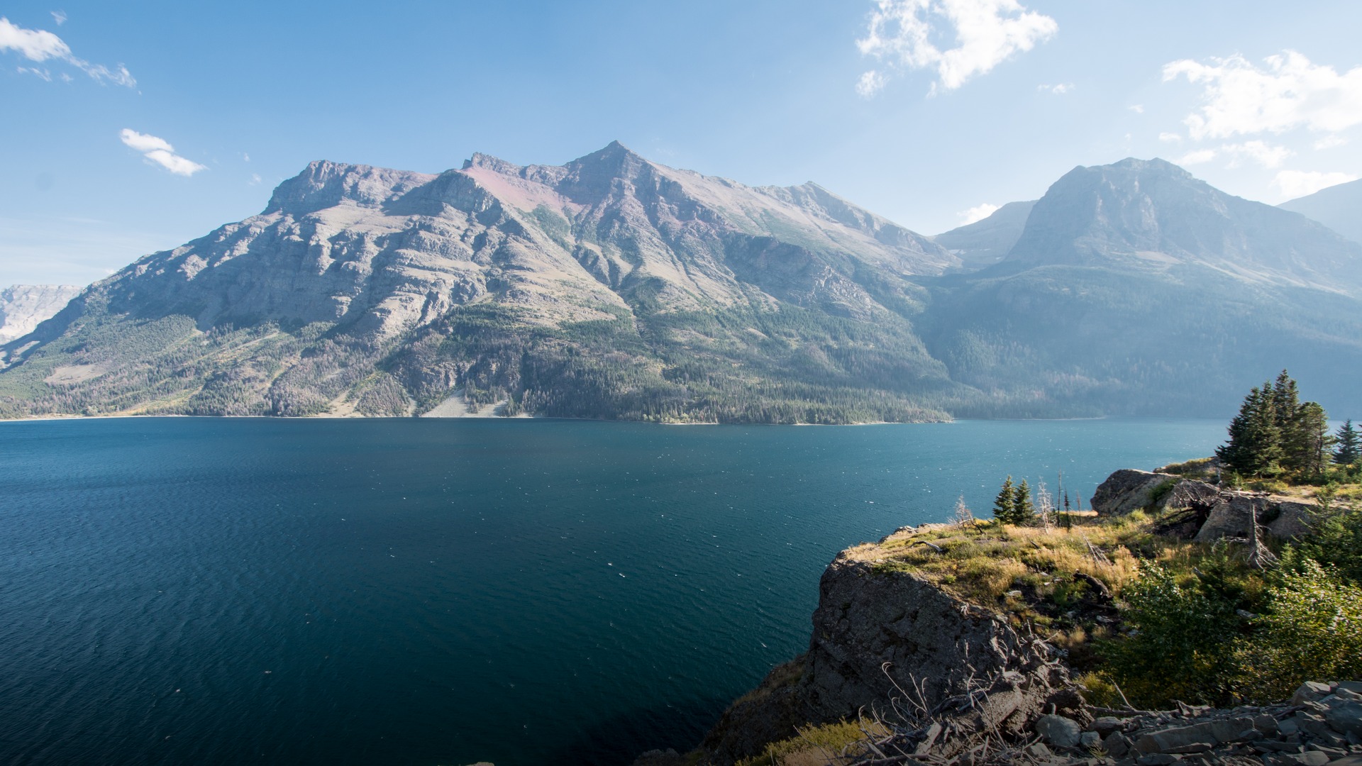 Scenic view of Saint Mary Lake with dramatic snow-streaked Rocky Mountain peaks reflecting in clear blue water in Glacier National Park, Montana.