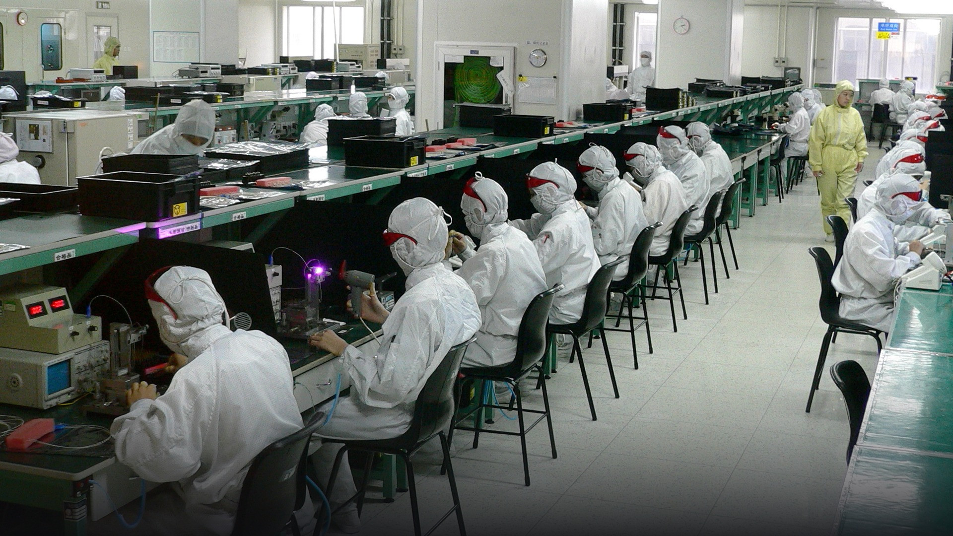 Expansive electronics manufacturing plant with assembly line workers in sterile uniforms.