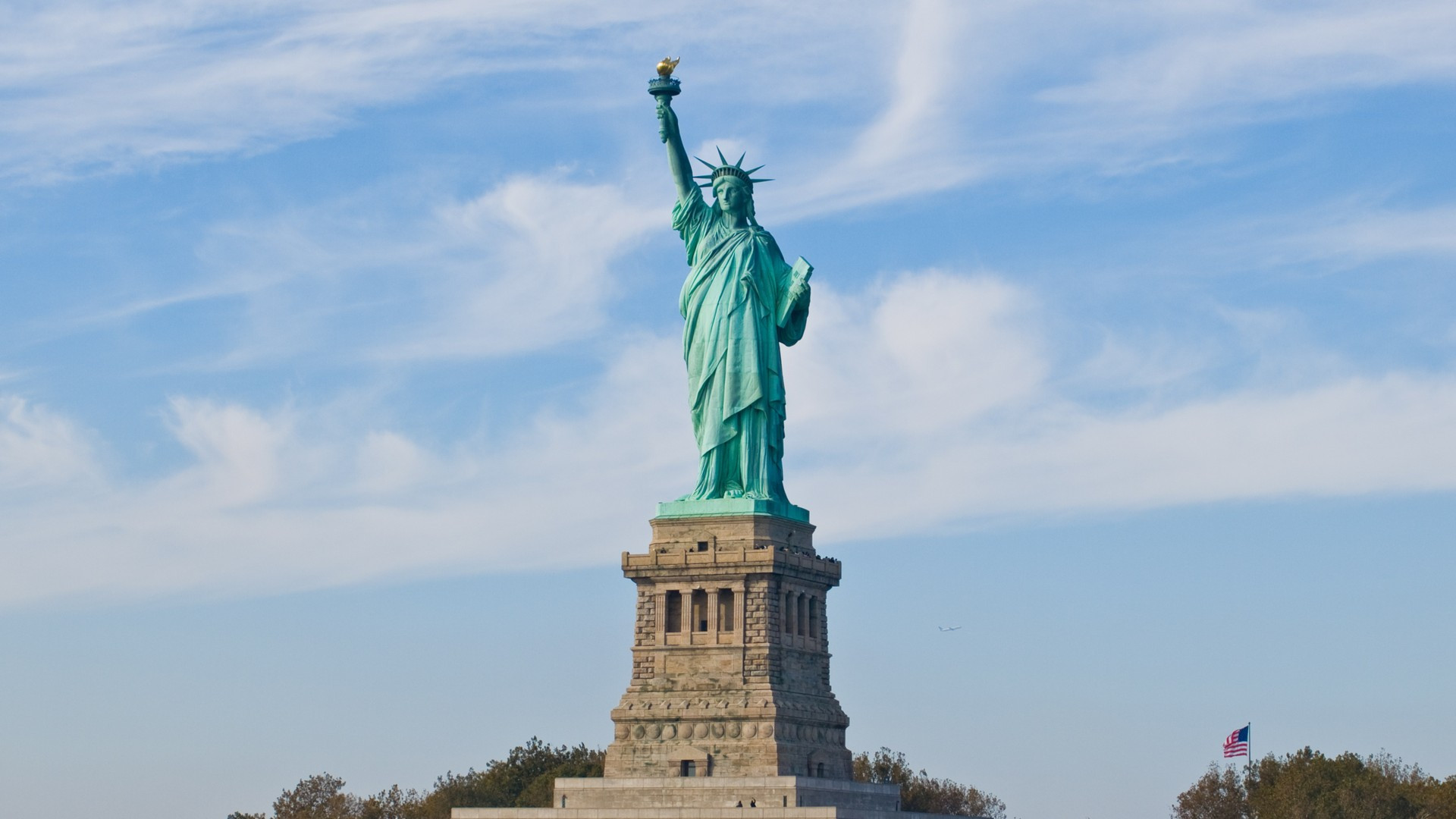 The Statue of Liberty holding her torch high against a blue sky over New York Harbor.