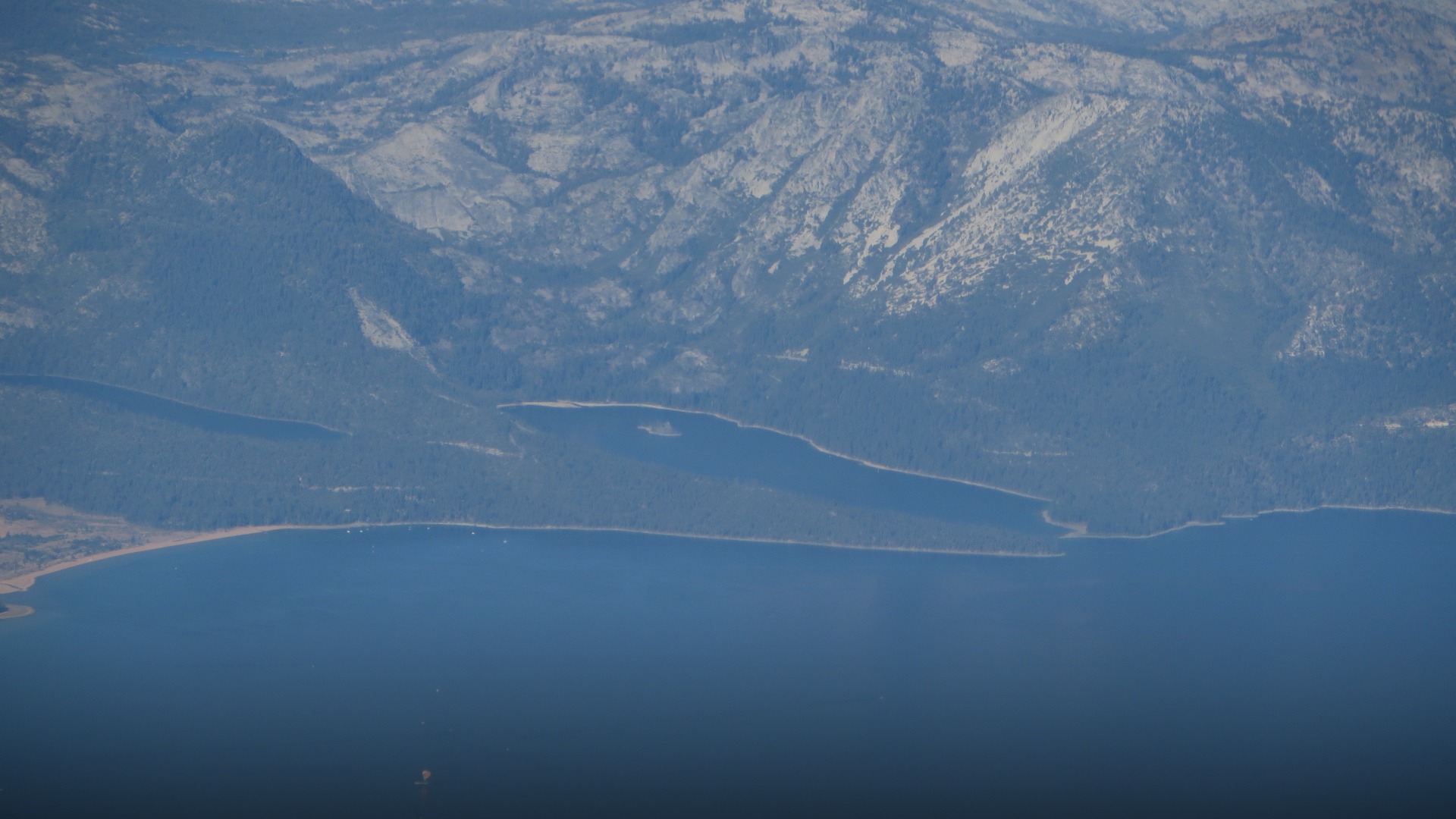 Scenic panoramic view of Emerald Bay in Lake Tahoe surrounded by snow-dusted evergreen forests and Sierra Nevada mountains.