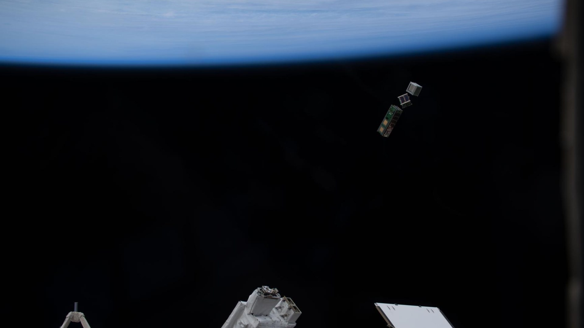 The curved blue horizon of Earth with small satellites deployed from the International Space Station