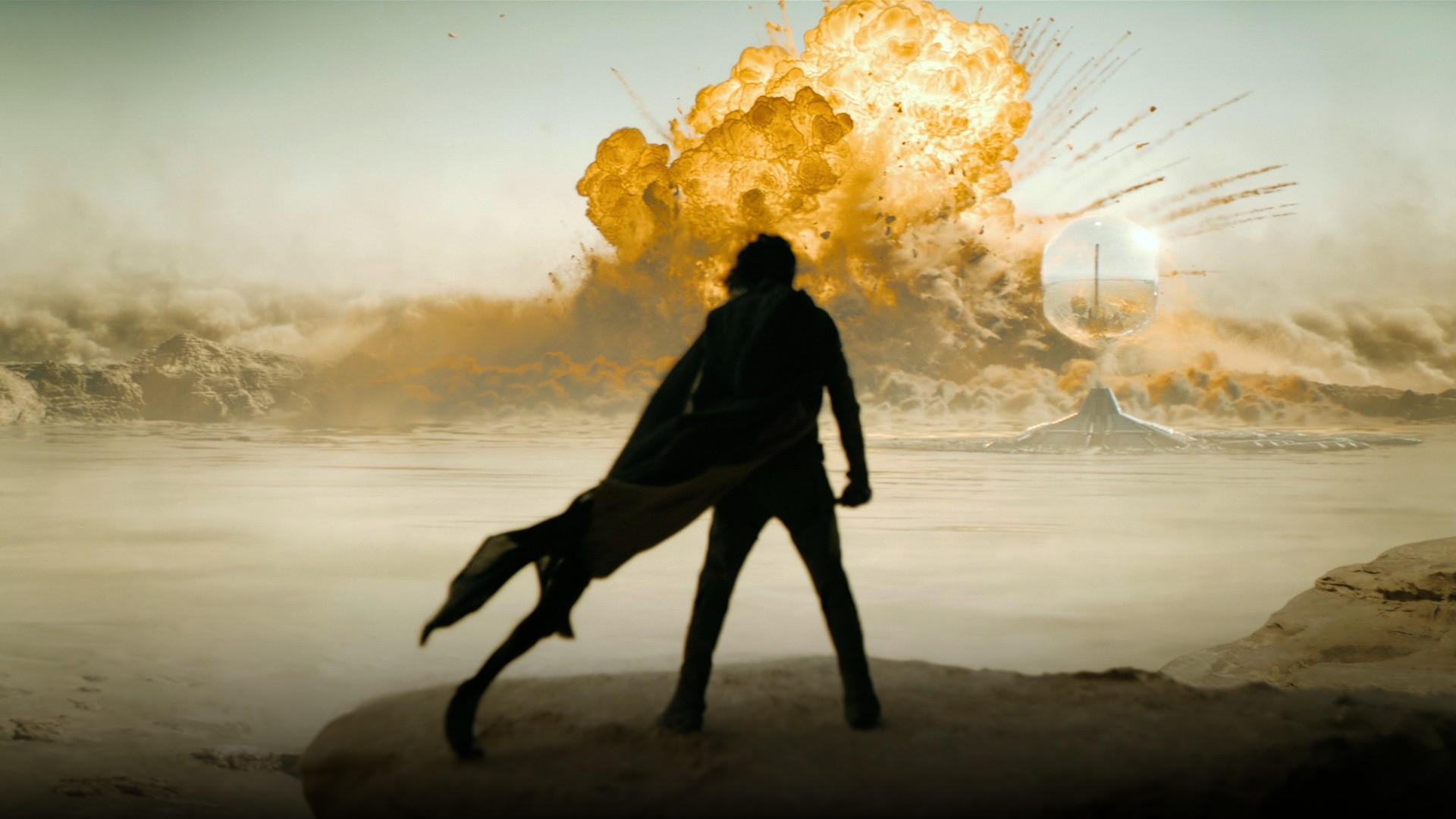 Paul Atreides silhouetted on a desert ridge with his cloak flowing as a massive spice harvester explosion erupts on Arrakis in Dune Part Two.