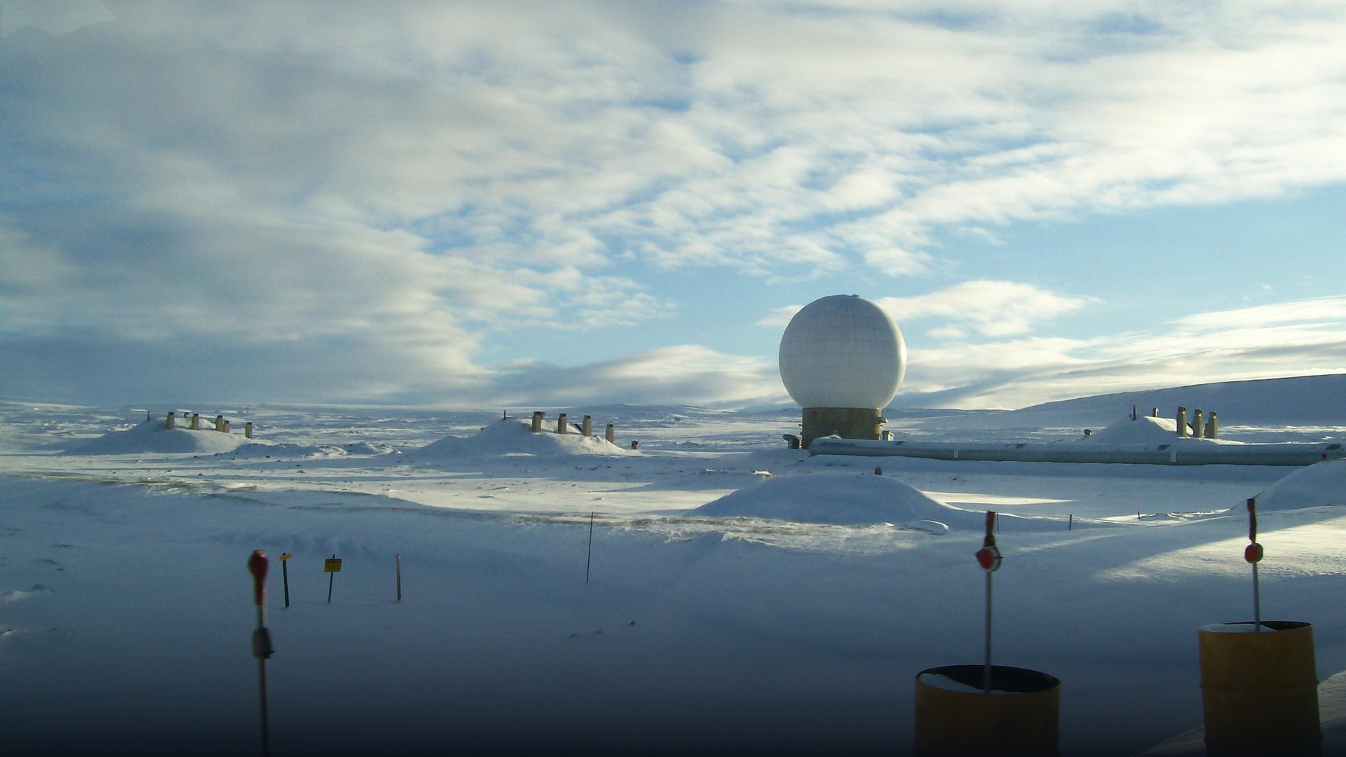 Large satellite tracking dish antenna dome under Arctic mountain terrain.