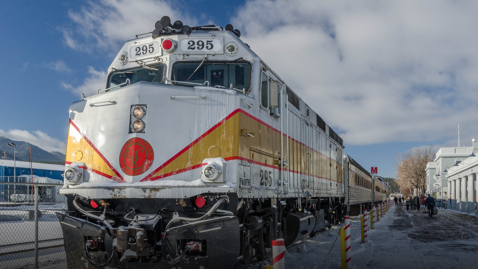 Grand Canyon Railway silver and gold locomotive arriving on snow-dusted tracks under a bright blue sky