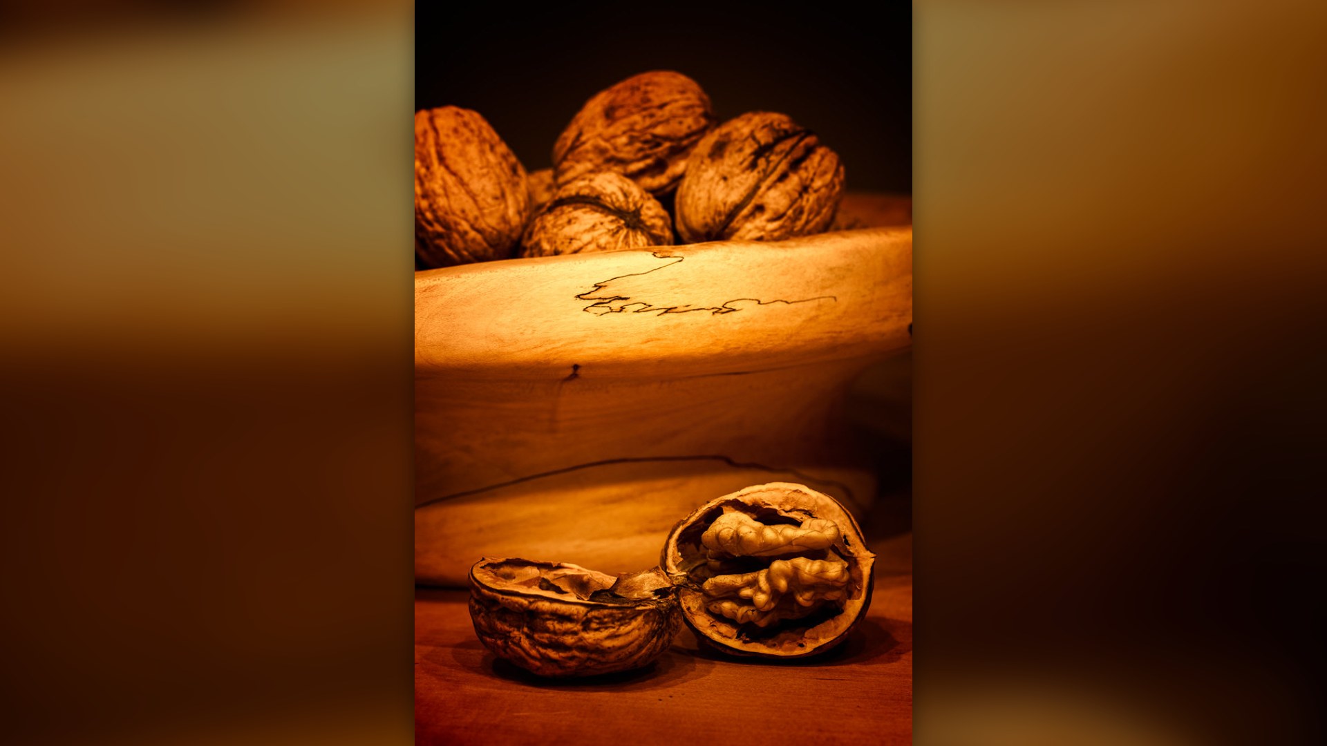 Whole and cracked walnuts in a wooden bowl with warm lighting