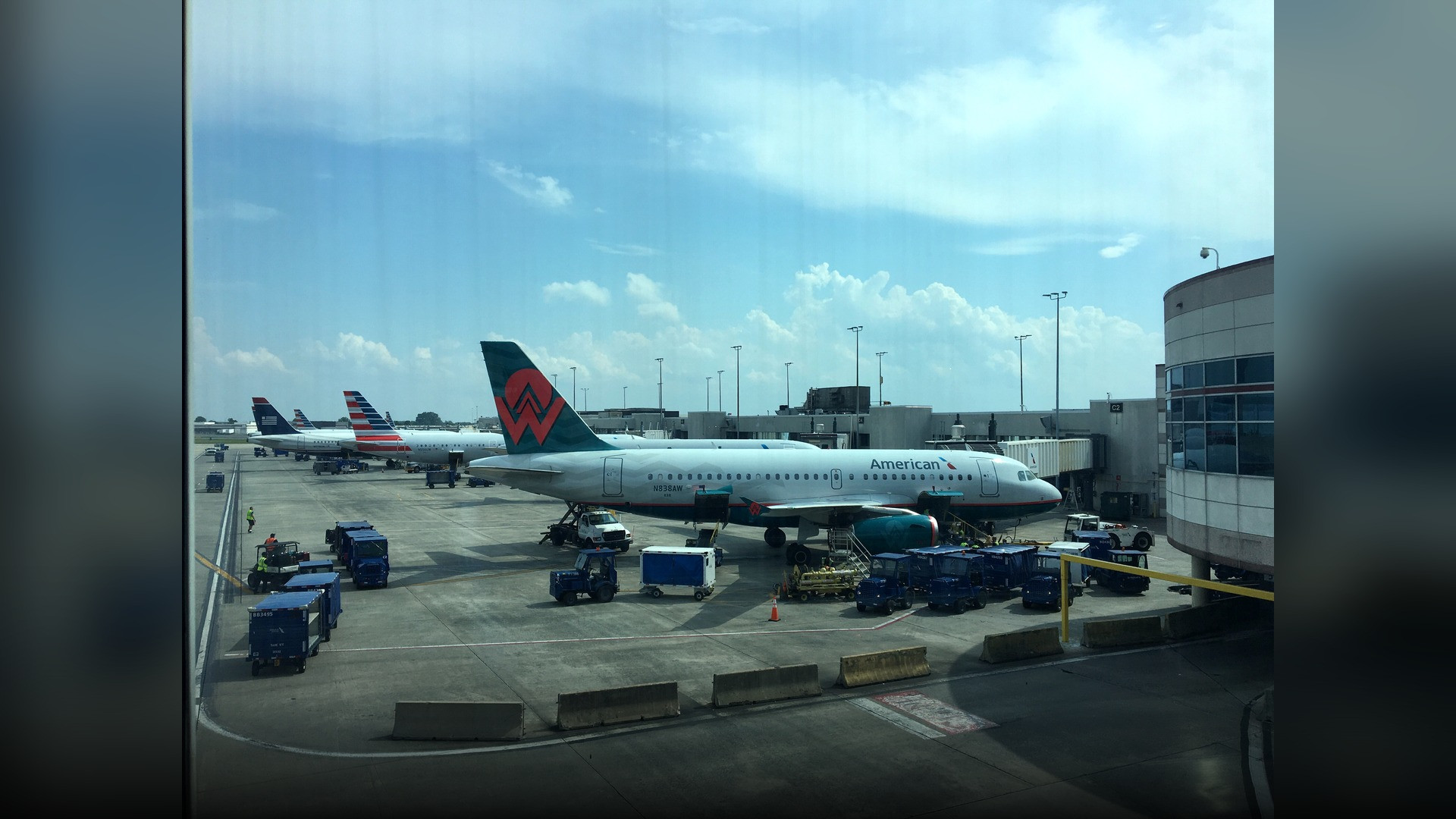 Aircraft taxiing in front of the modern passenger concourses and control tower at Charlotte Douglas International Airport.