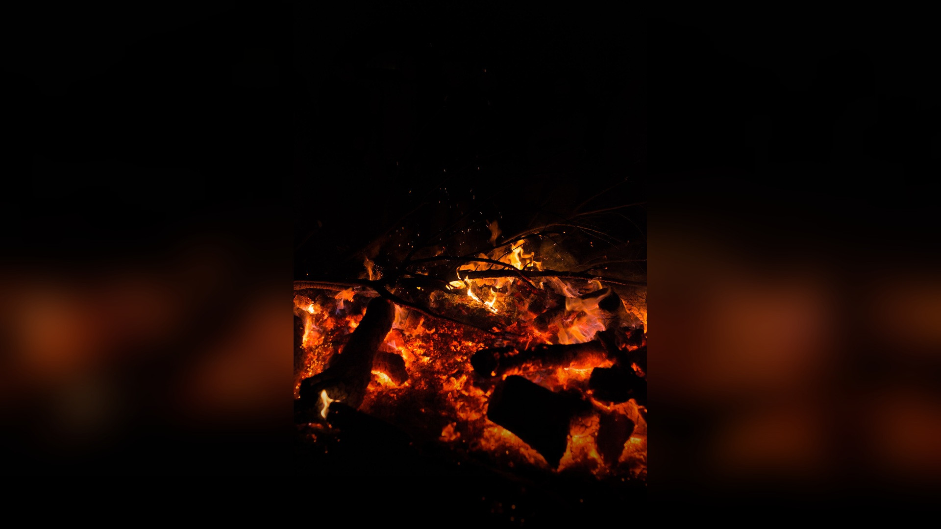 A towering ceremonial bonfire with intense orange and golden flames roaring into the night sky.