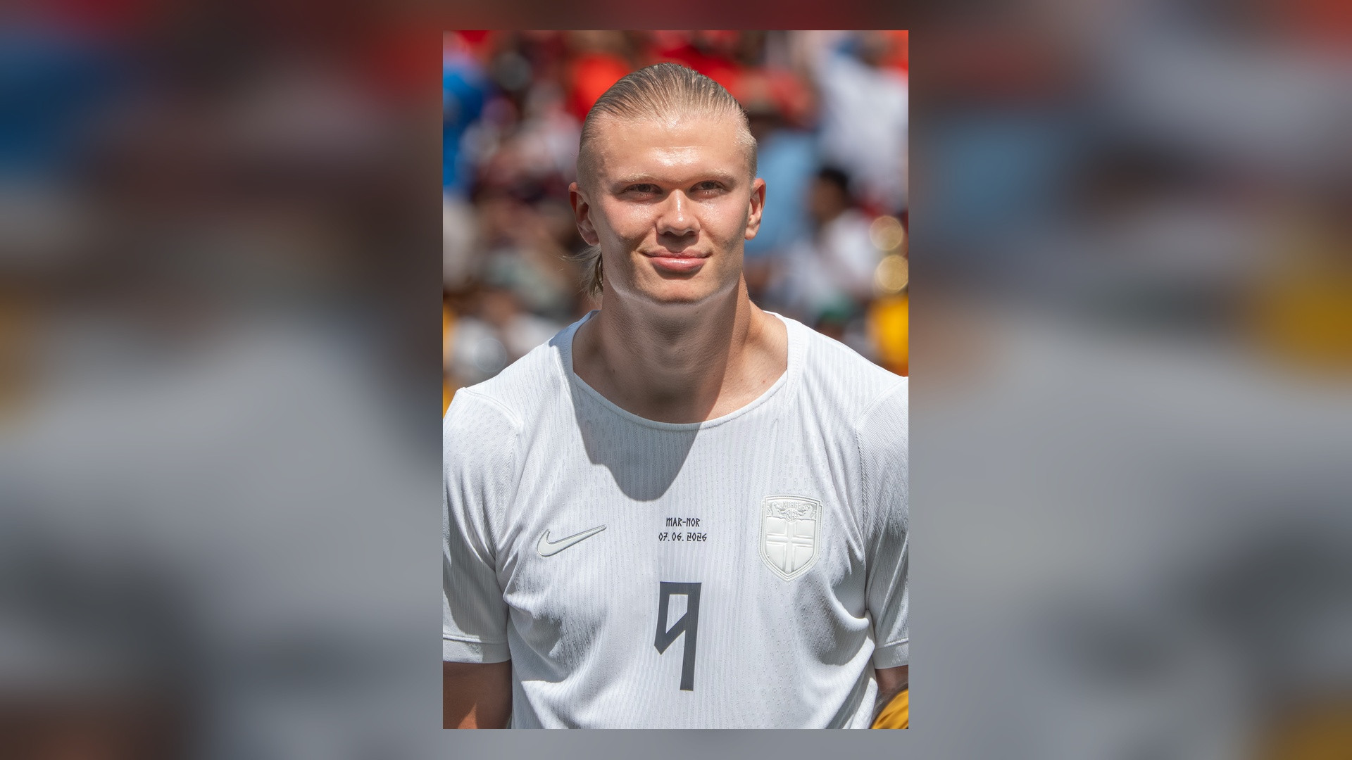 Close-up photograph of Erling Haaland in white kit smiling.