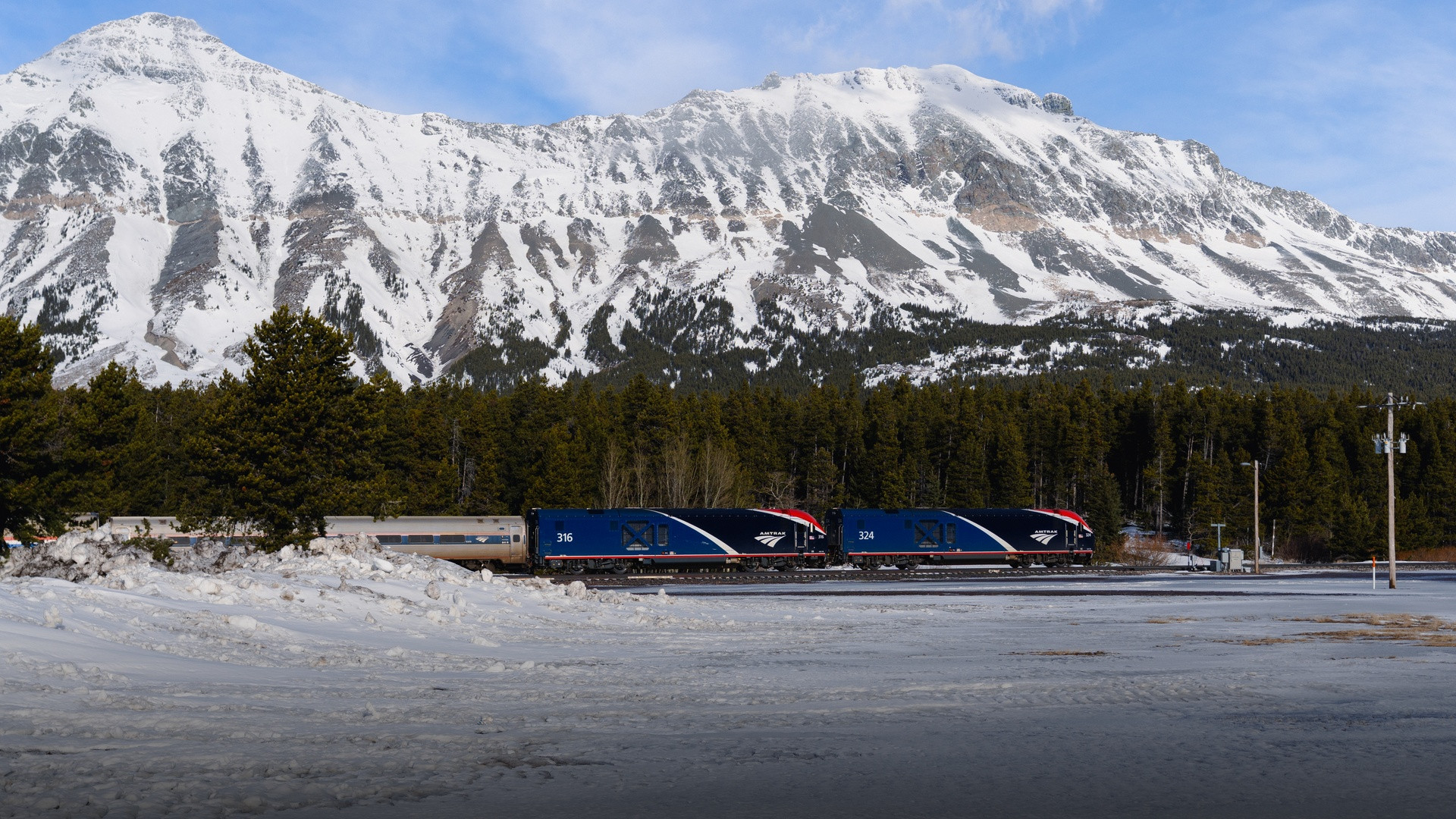 Amtrak Empire Builder diesel locomotive traveling across snow-covered tracks beneath the rugged Rocky Mountains