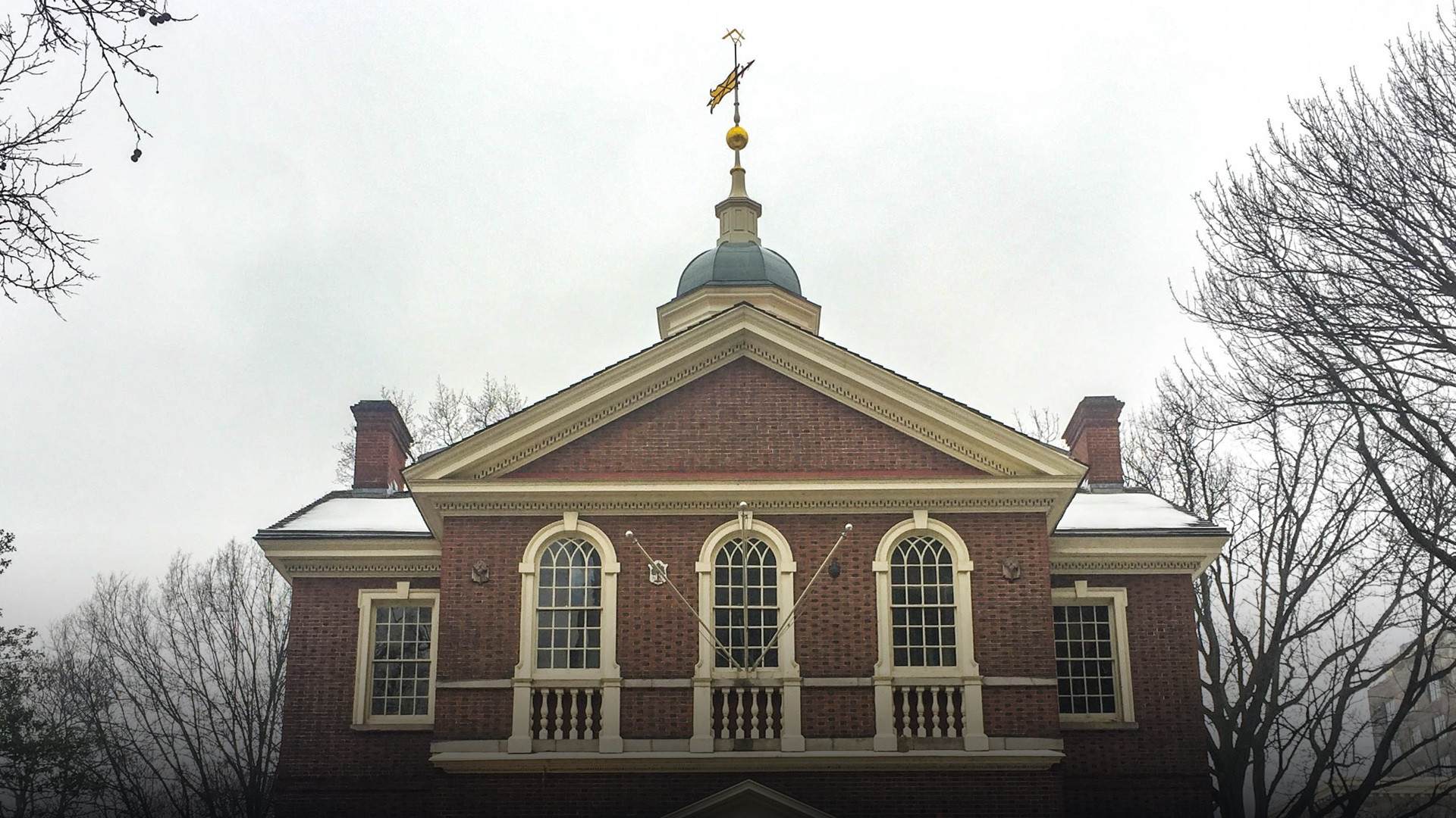Independence Hall in Philadelphia viewed across snow-covered lawns and bare winter trees.