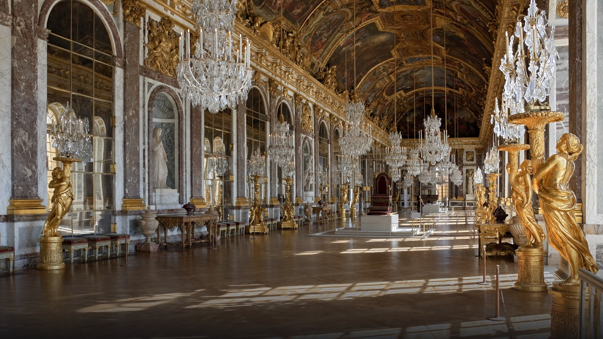 Gilded chandeliers and arched mirrors lining the famous Hall of Mirrors at Versailles.