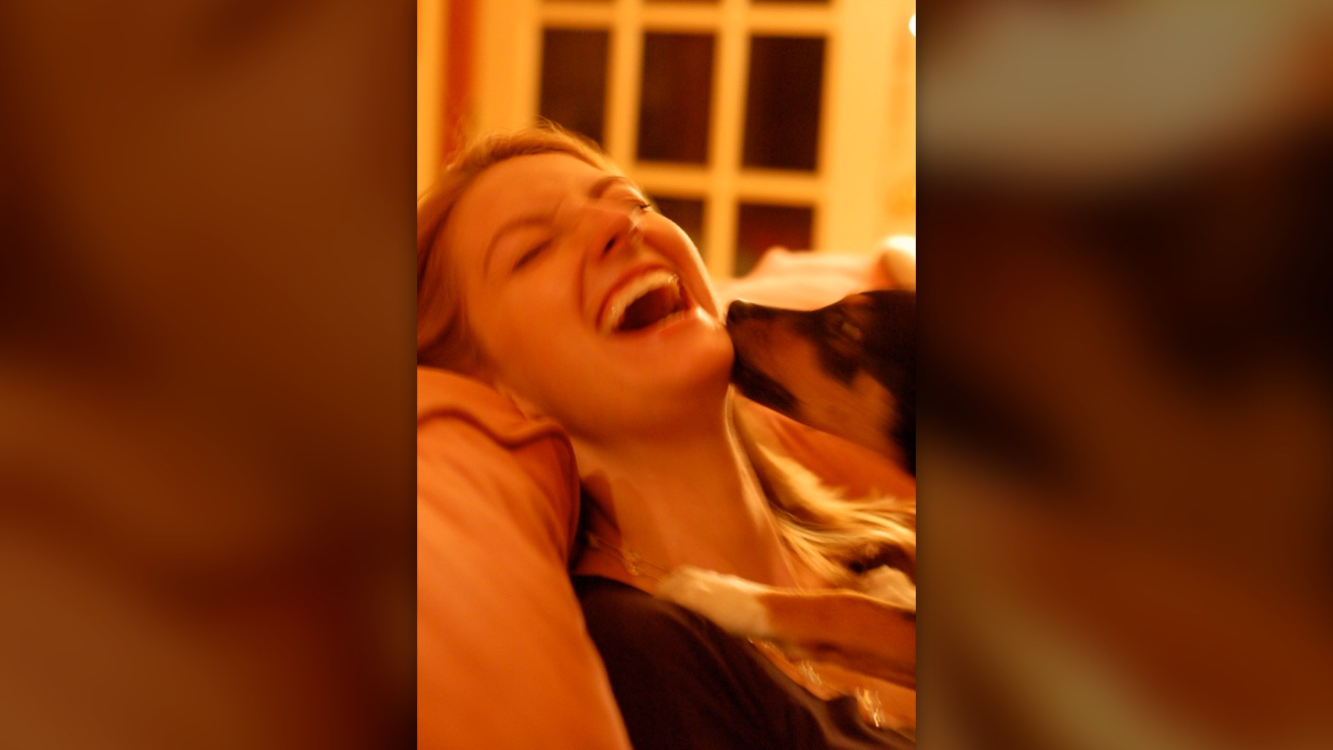 A puppy affectionately licking the face of a laughing woman