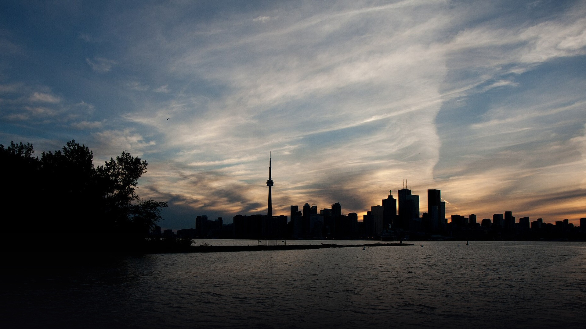 Toronto skyline at sunset with the CN Tower standing prominent against the orange sky.