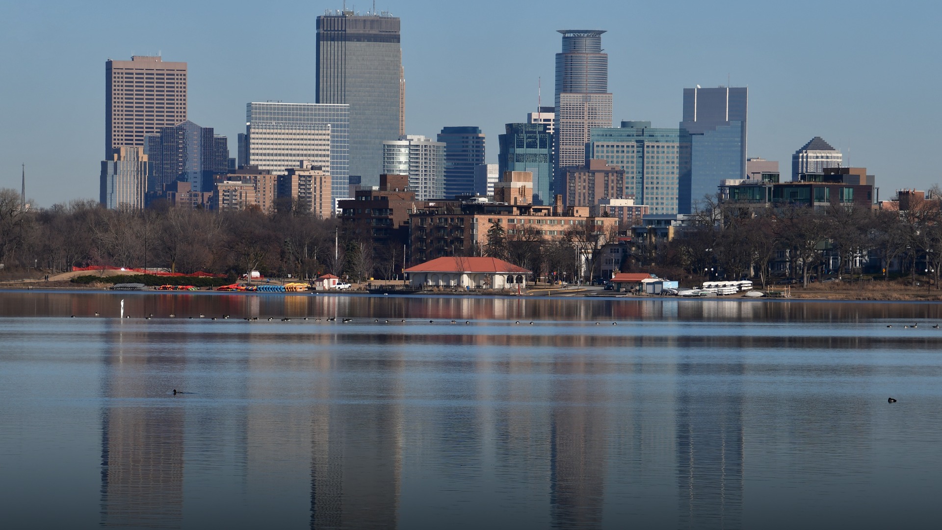 Vibrant lakeside view of Lake Calhoun with park visitors enjoying outdoor recreation in front of the downtown Minneapolis skyline.