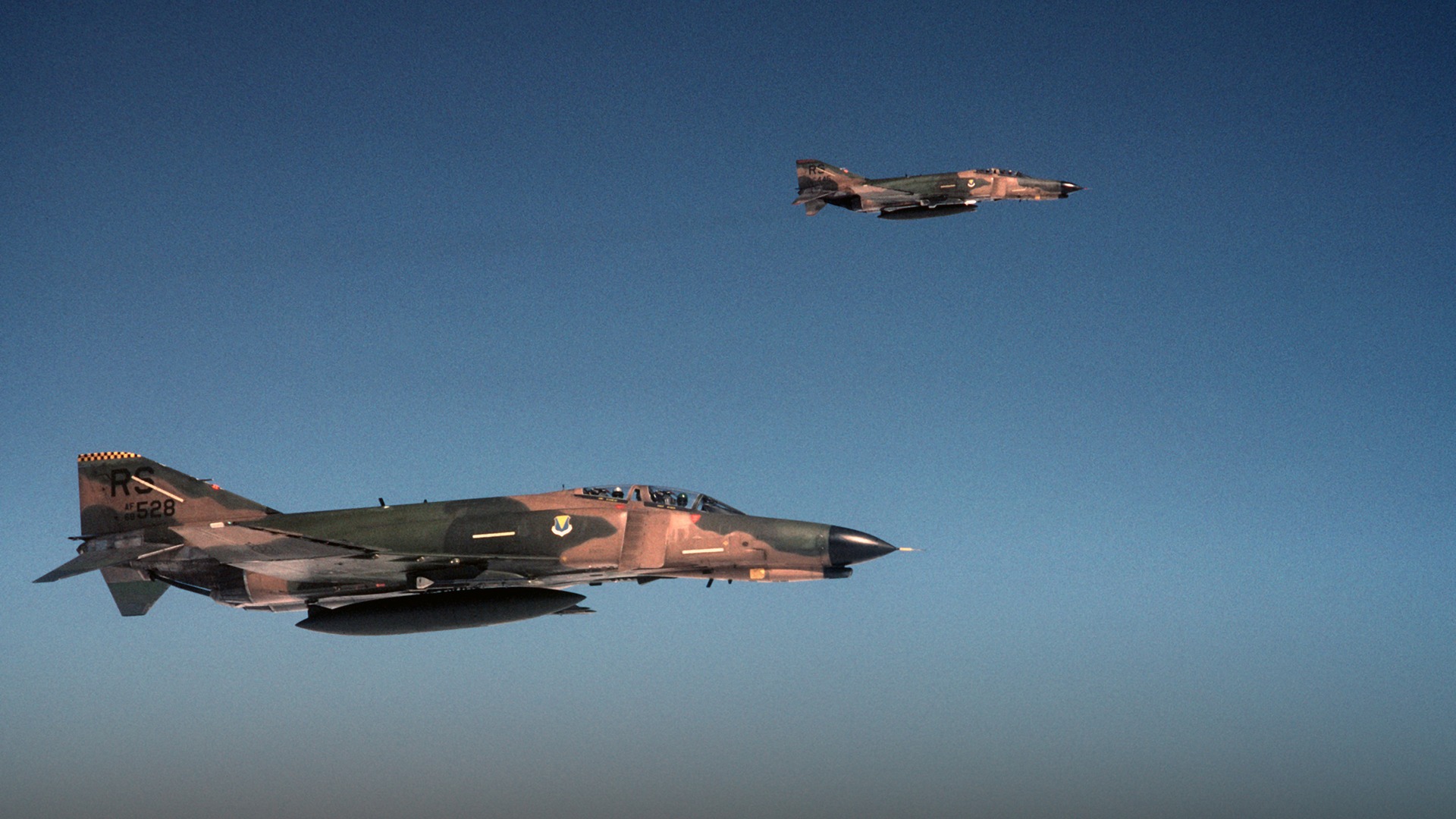 Pair of camouflaged USAF F-4E Phantom II supersonic heavy fighters flying in formation.