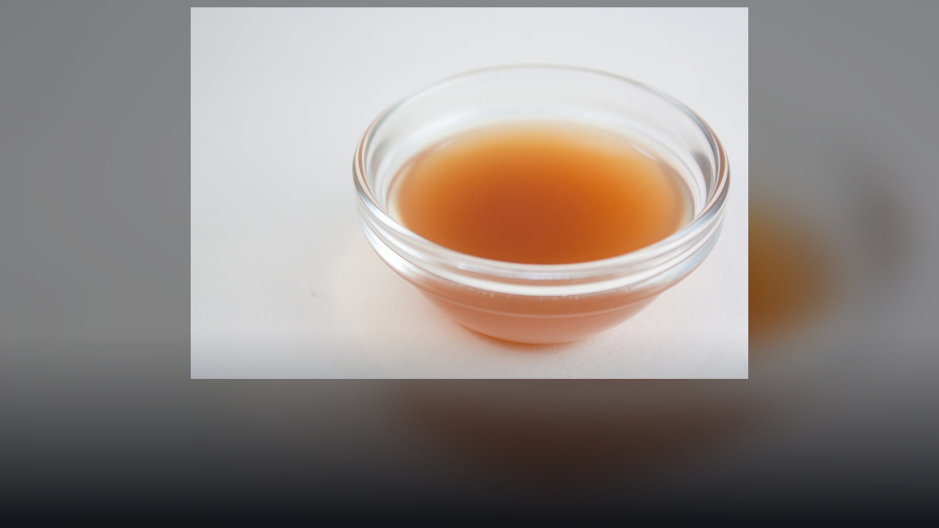 Bright golden bottle of organic apple cider vinegar surrounded by crisp fresh red apples on a well-lit table.