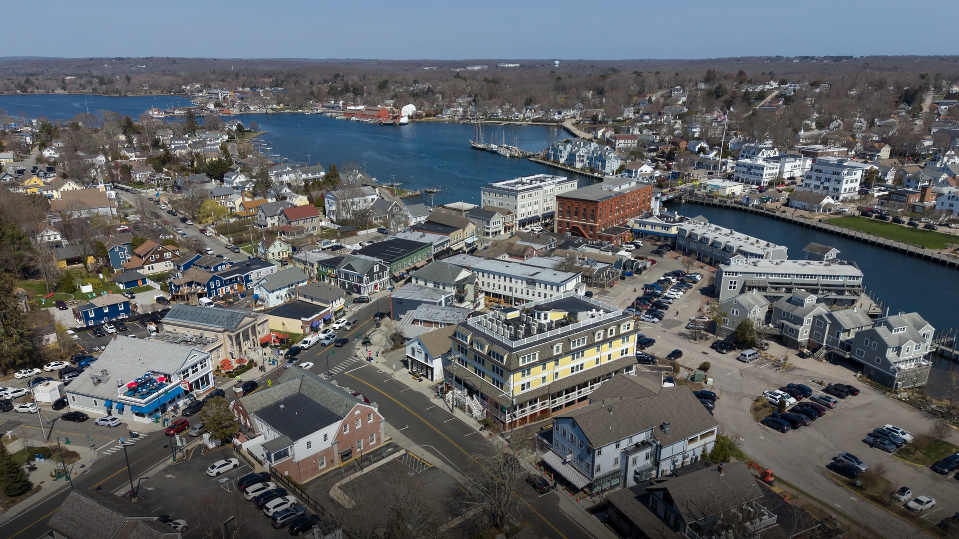 Aerial view of the coastal town of Mystic Connecticut showing the historic riverfront harbor, boats, and lush green surrounding landscape.