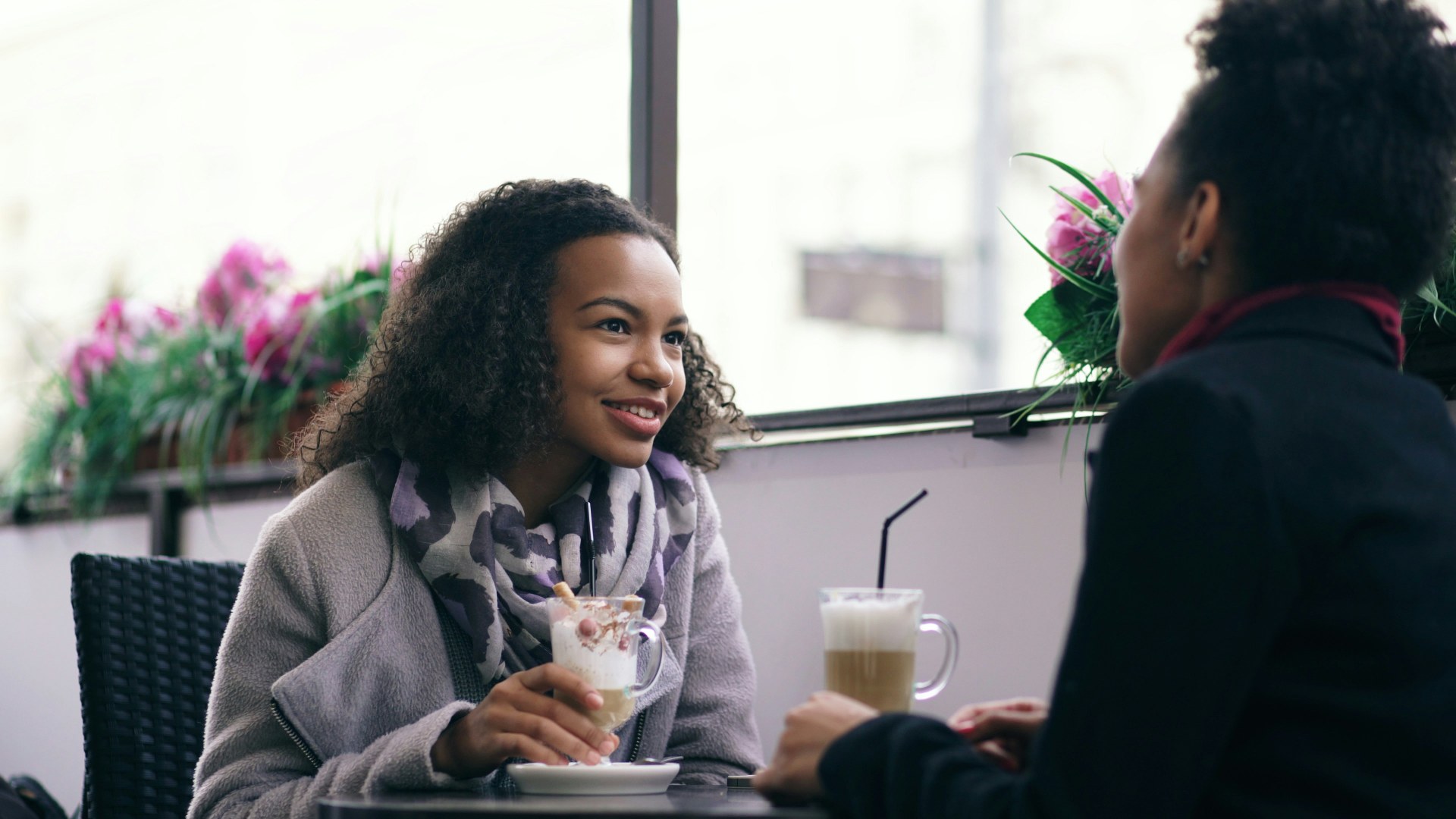 Two women talking at a cafe with drinks while exchanging a forced smile
