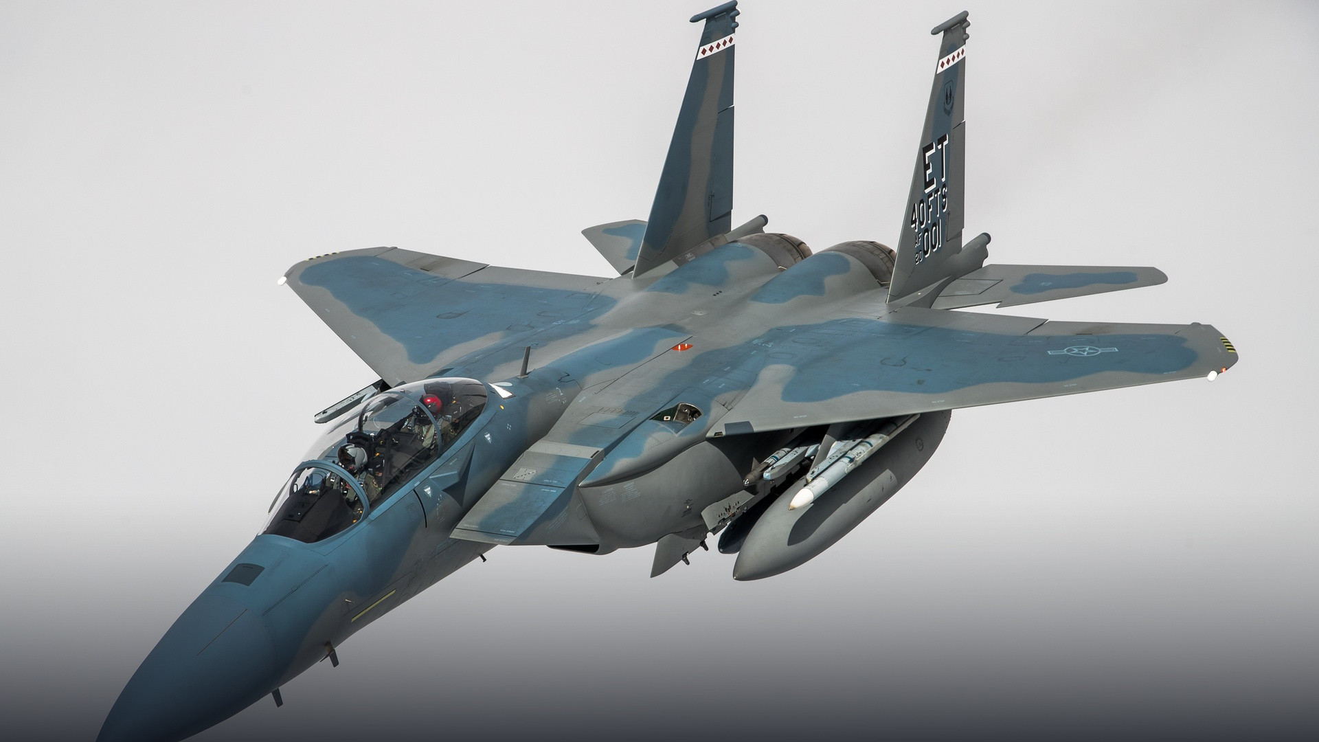 Boeing F-15EX Eagle II heavyweight fighter jet banking aggressively in flight with pilot visible in cockpit.