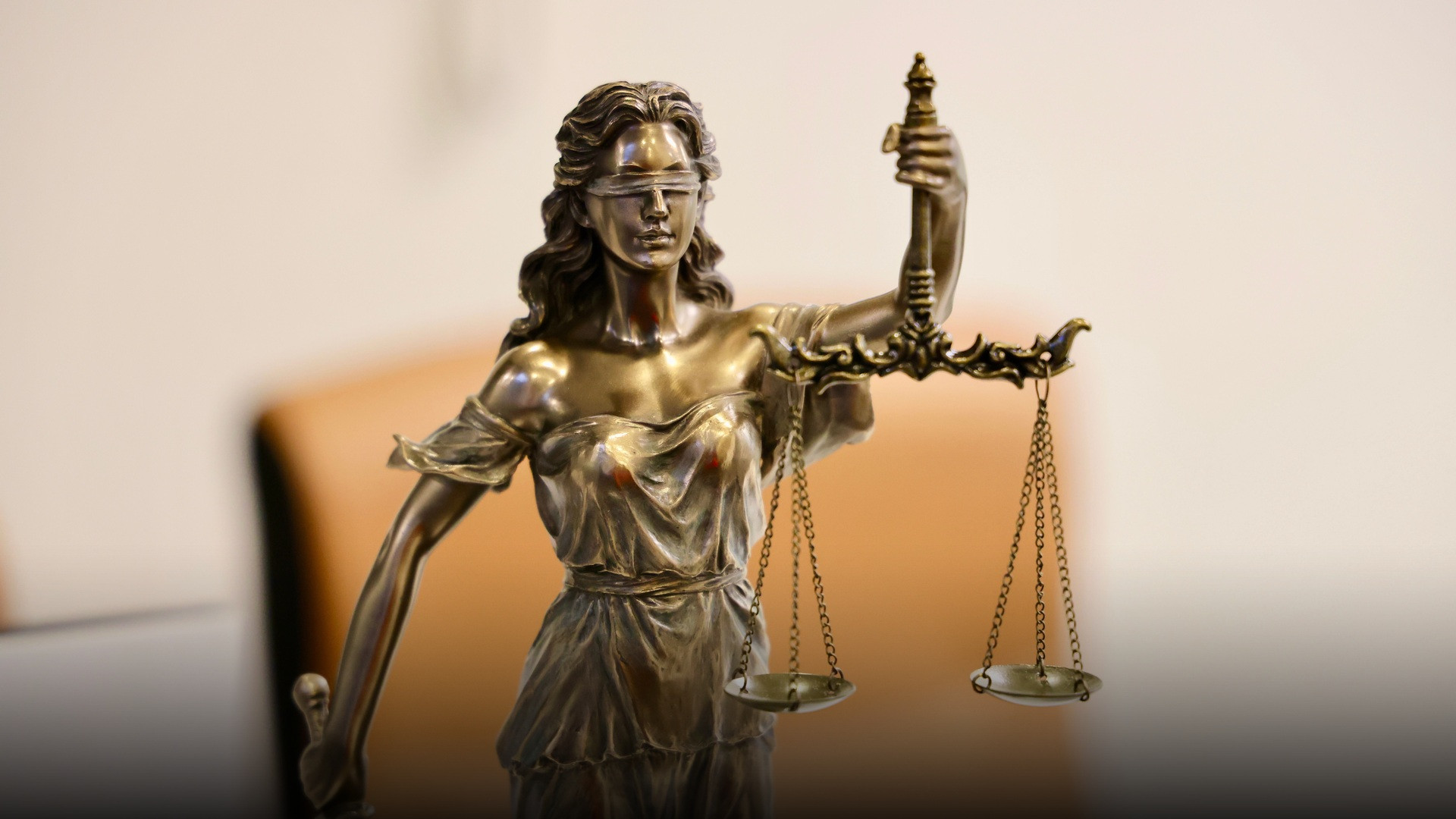 A bronze statue of Lady Justice blindfolded and holding the balanced scales of justice in a courtroom.