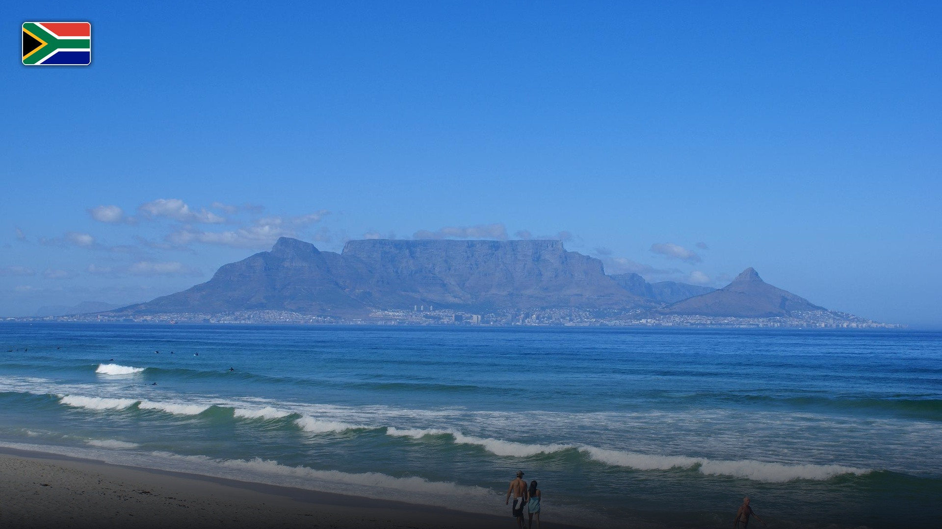 Scenic panoramic view of Table Mountain rising across Table Bay from Bloubergstrand, with the flag of South Africa.
