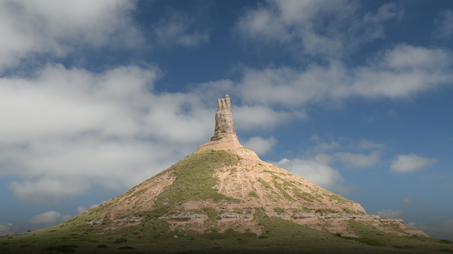 Iconic natural geological spire of Chimney Rock rising against a blue sky with clouds in western Nebraska.