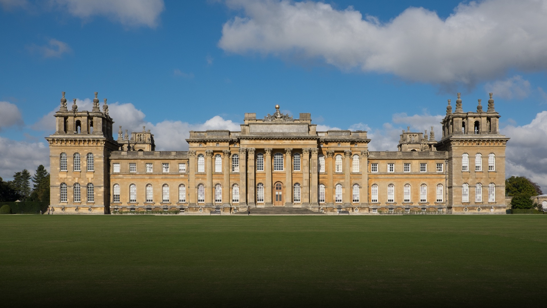The monumental Baroque facade and colonnades of Blenheim Palace across expansive open lawns.