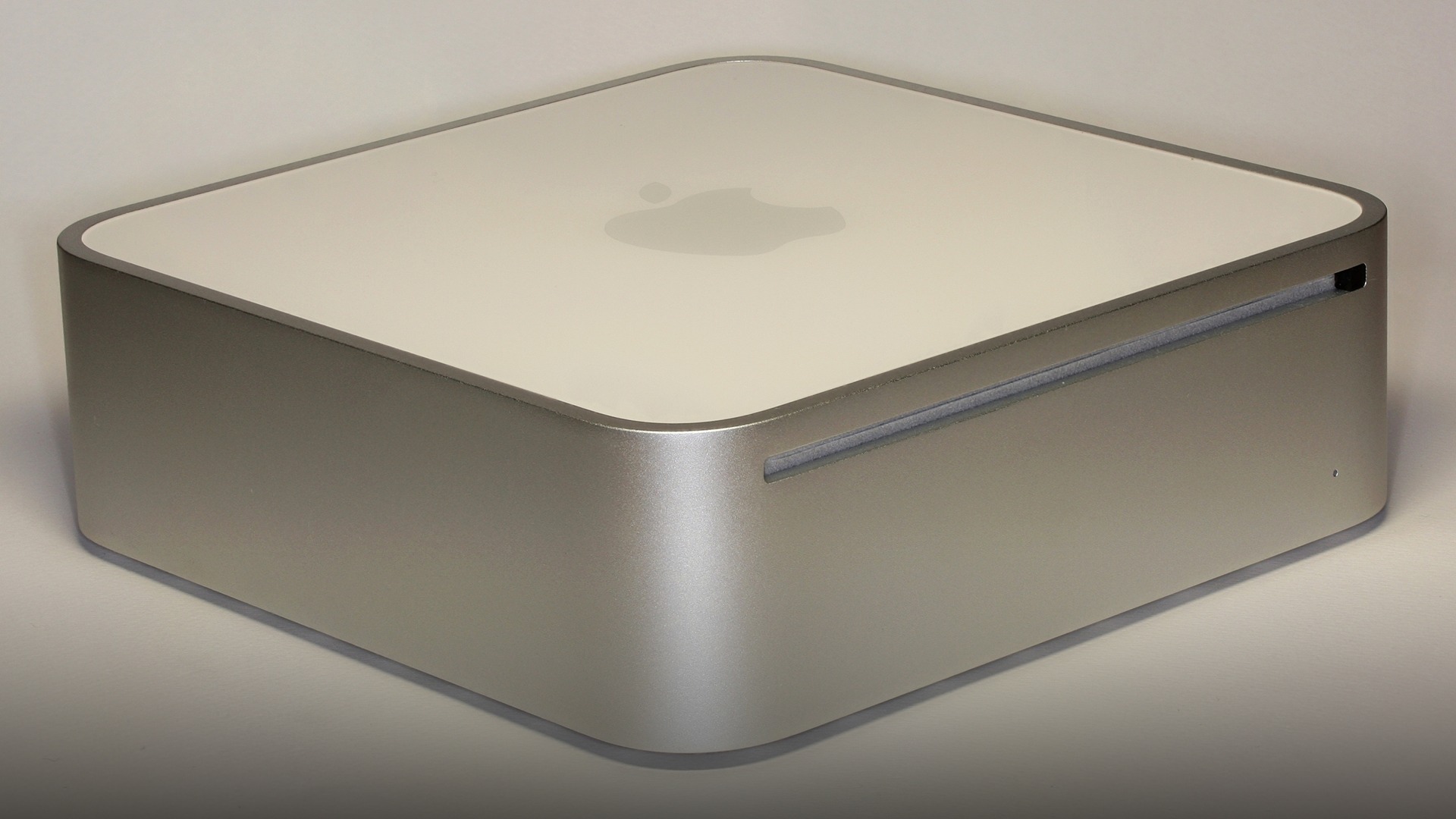 Silver aluminum Apple Mac mini desktop computer shown on an office desk beside an external monitor.