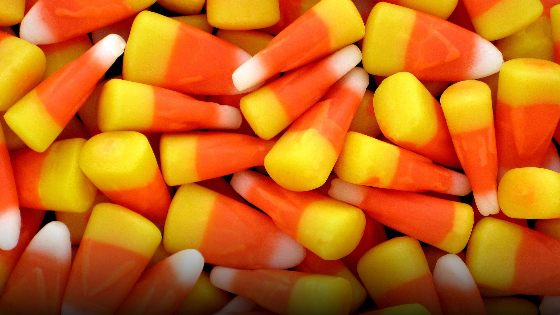 A clean studio arrangement of classic yellow, orange, and white triangular candy corn kernels.
