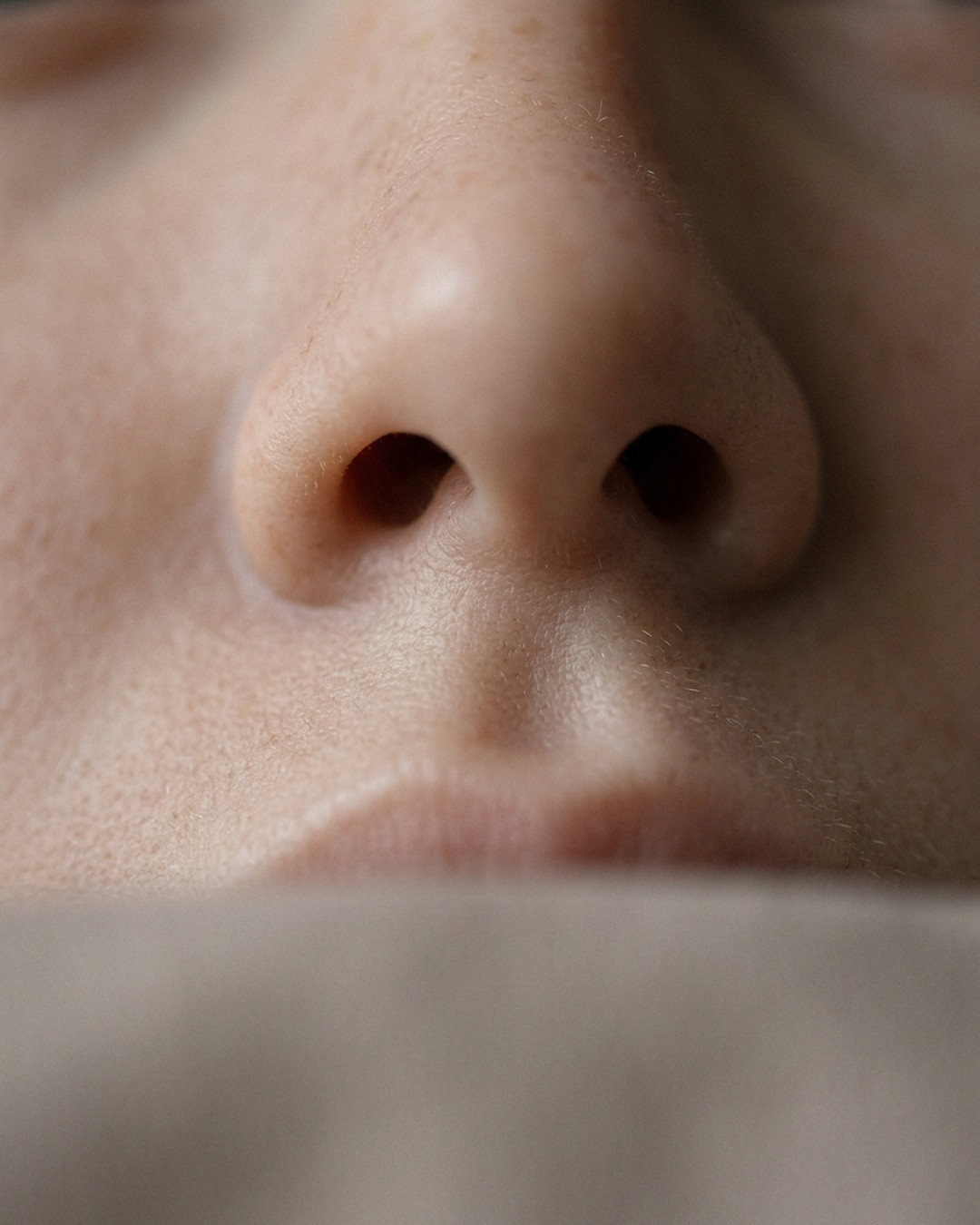 Subtle upward angle close-up of the tip and underside of a nose showing the strip of tissue between the nostrils.