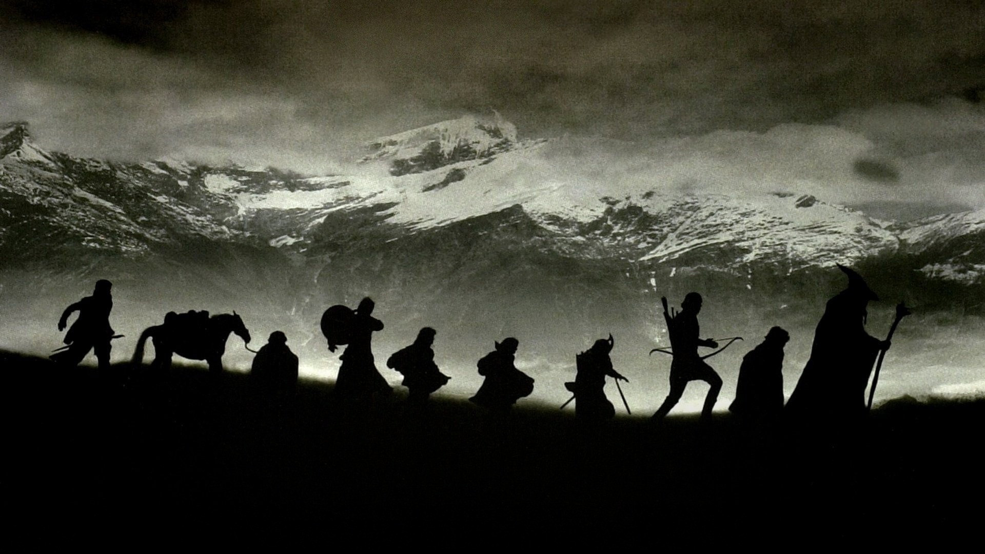 The Fellowship of nine companions treks across a rugged alpine mountain ridge against snowy peaks in The Lord of the Rings.