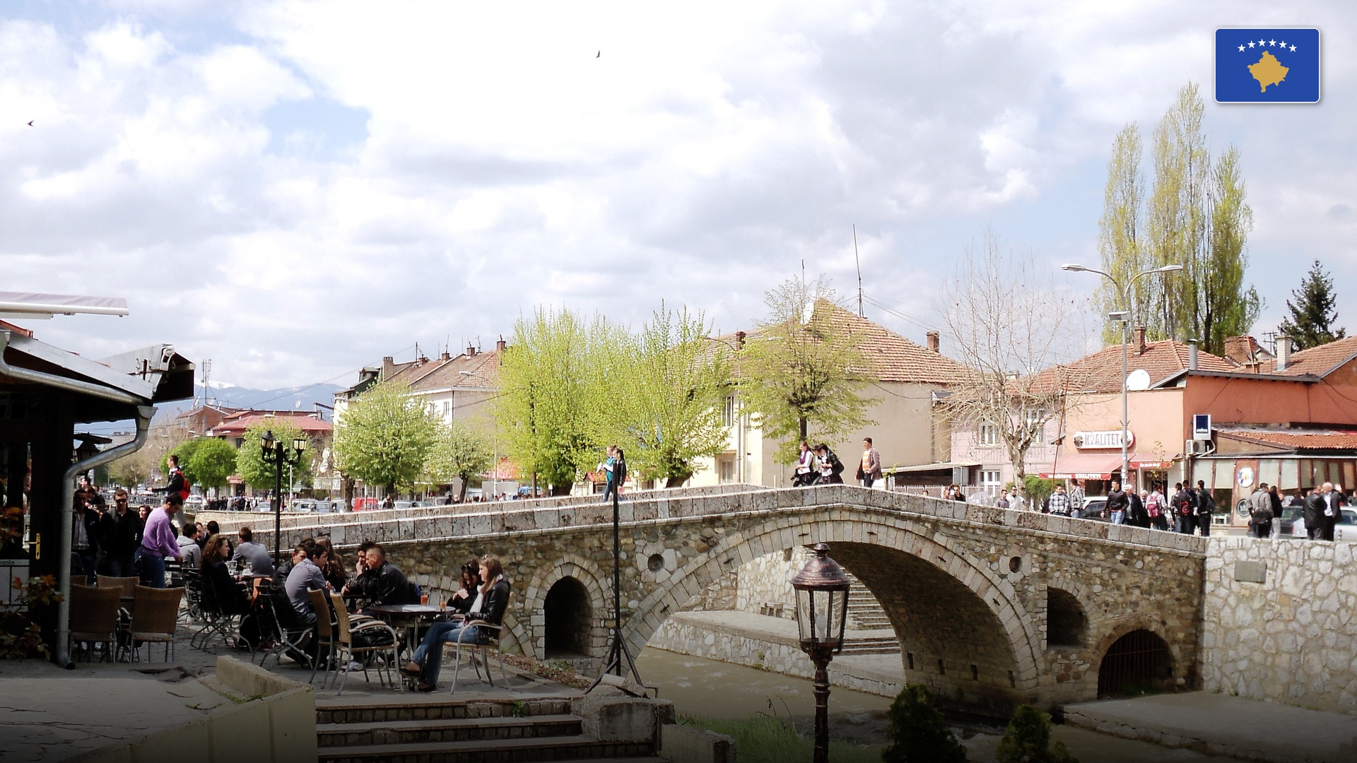 Historic Ottoman stone bridge in Prizren spanning the Bistrica river with waterside cafes and streetlamps.