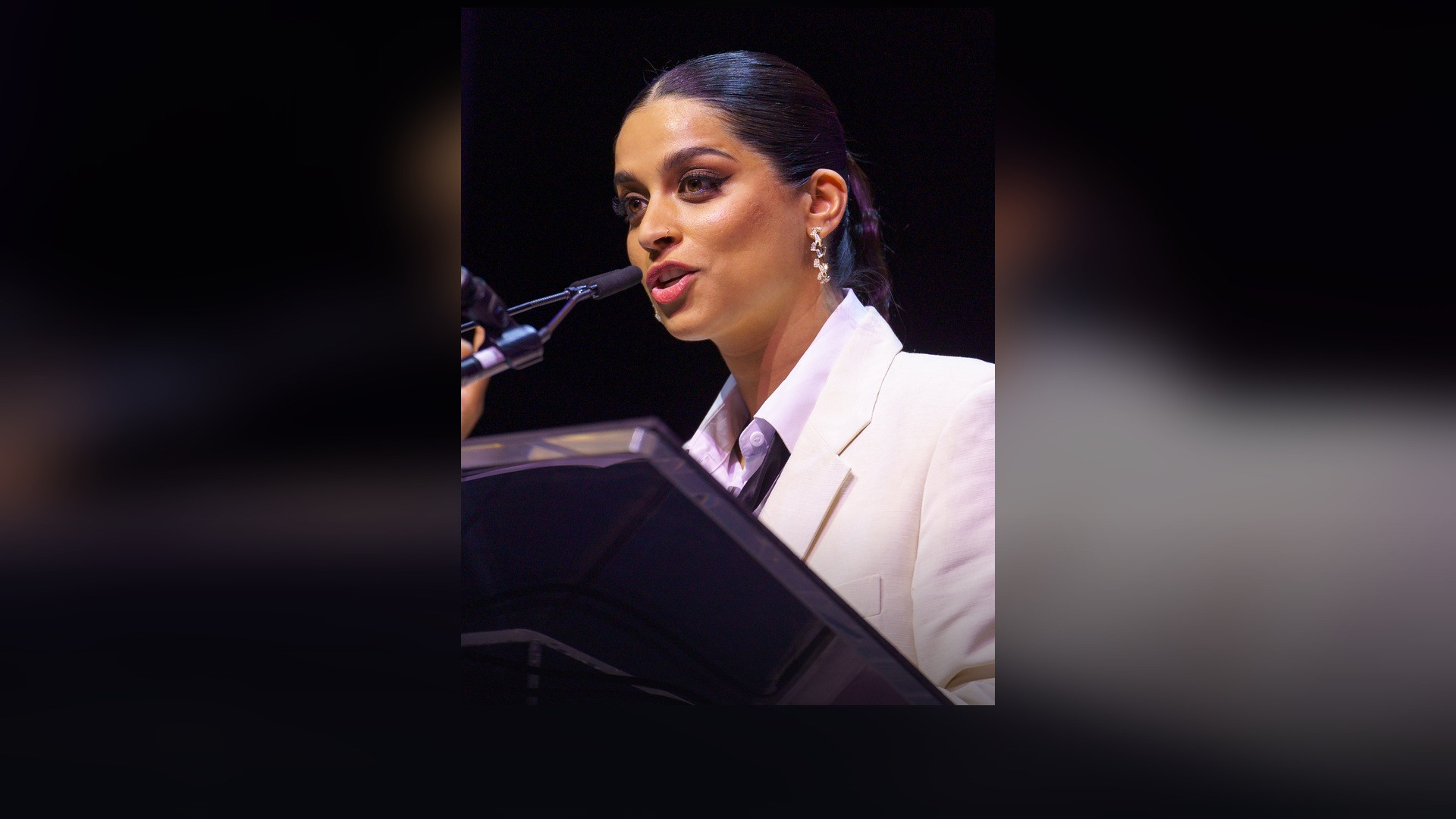 Lilly Singh speaking at the 2024 SXSW Variety Comedy Awards in a white suit.