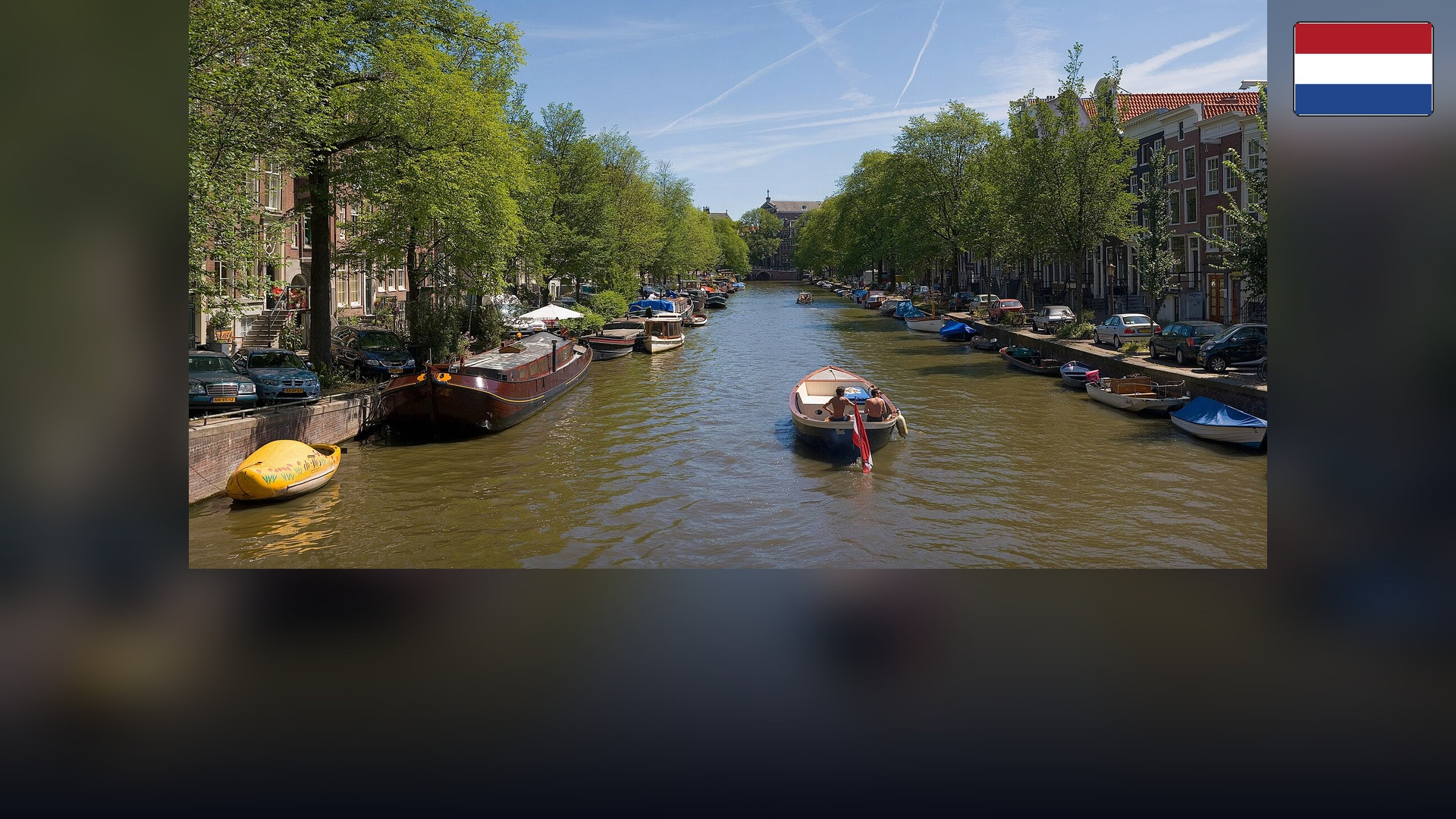 Historic canal houses and bridges in Amsterdam with the Dutch flag in the top right corner.