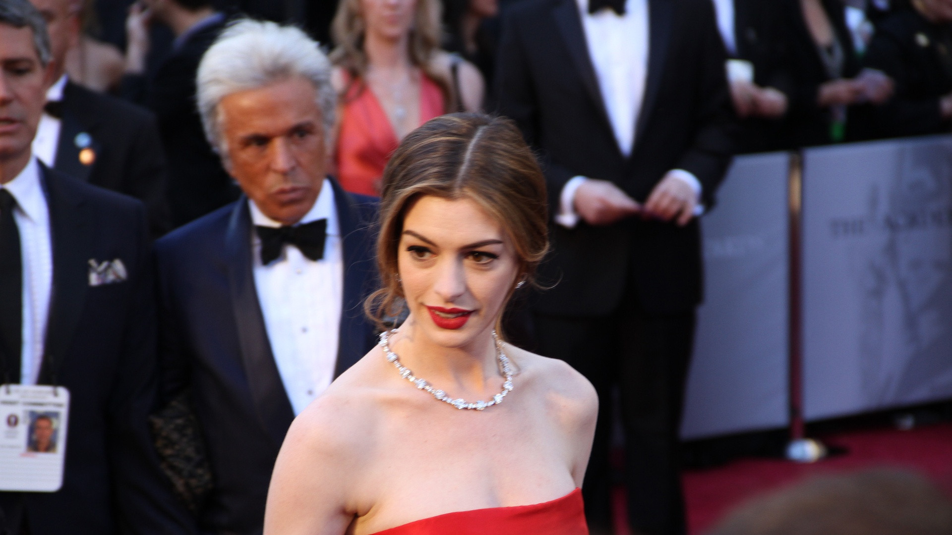 Anne Hathaway on the red carpet at the Academy Awards in a vintage red gown with radiant smile.