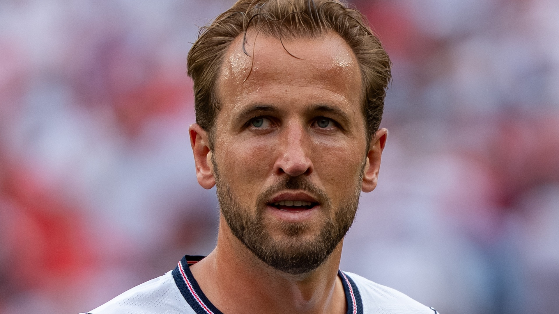 Close-up photograph of Harry Kane in his white England international kit, head and shoulders visible against a stadium crowd.