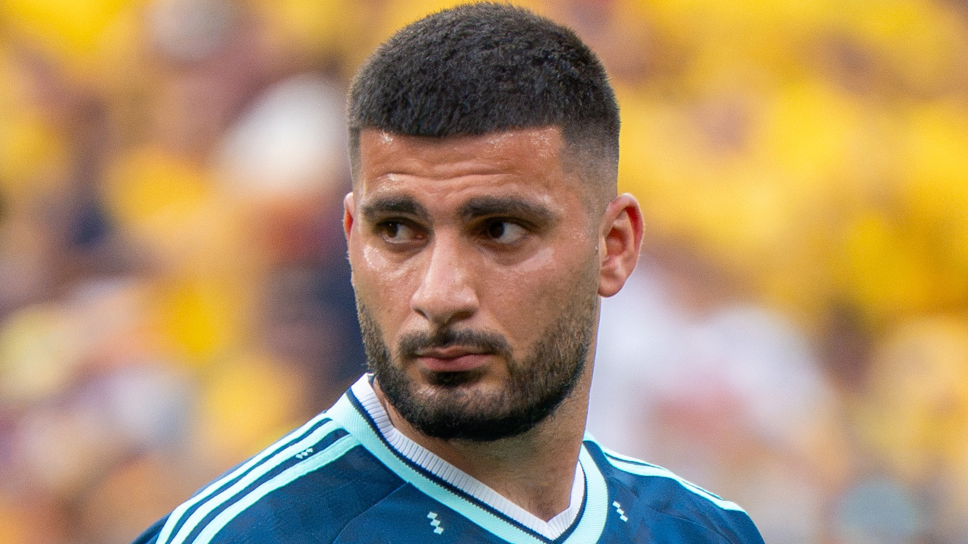 Close-up photograph of Deniz Undav with short dark beard and dark jersey looking across the pitch.