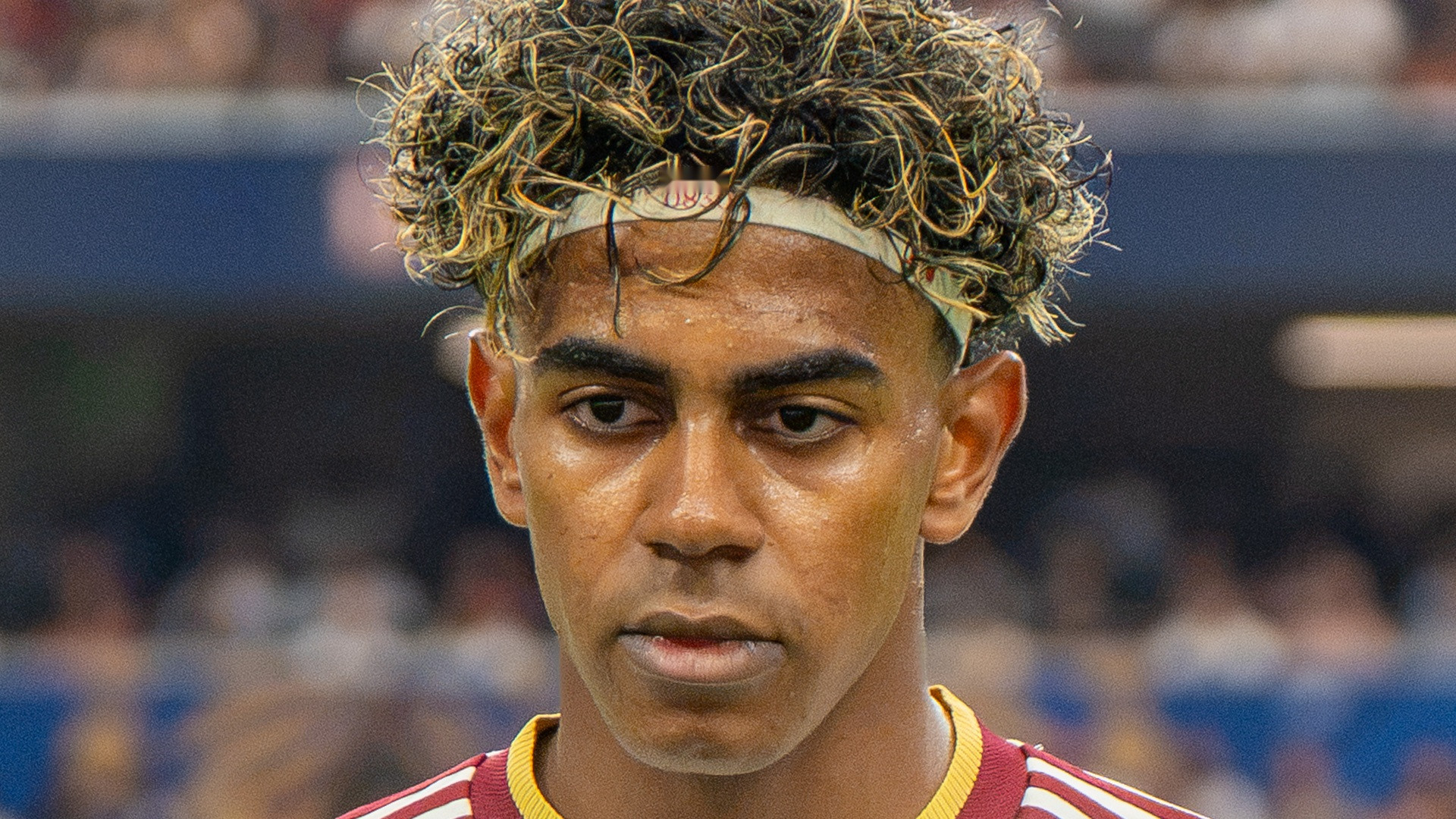 Close-up portrait of young Lamine Yamal with curly frosted hair and sports headband looking forward.