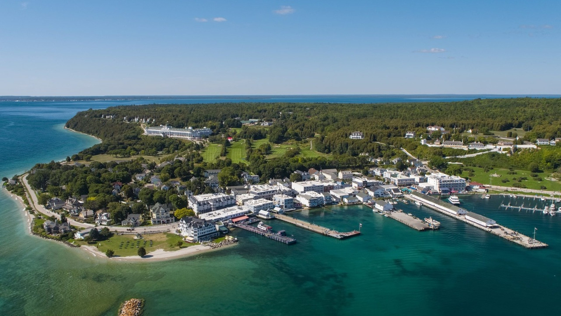 Classic horse-drawn carriages carrying visitors past charming pastel Victorian storefronts on Mackinac Island.